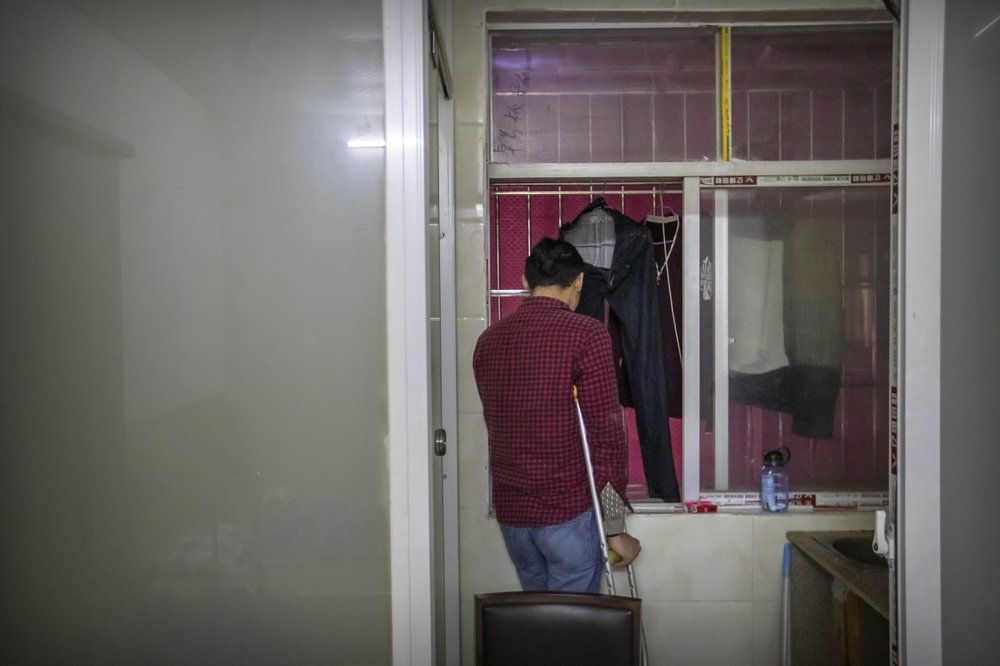 In this Dec. 6, 2019, photo, Wu Yi, who has struggled with Oxycontin abuse, smokes a cigarette while looking out the window of his rented room in Shenzhen in southern China's Guangdong Province. Officially, pain pill abuse is an American problem, not a Chinese one. But people in China have fallen into opioid abuse the same way many Americans did, through a doctor's prescription. And despite China's strict regulations, online trafficking networks, which facilitated the spread of opioids in the U.S., also exist in China. Image by Mark Schiefelbein/ AP Photo. China, 2019.