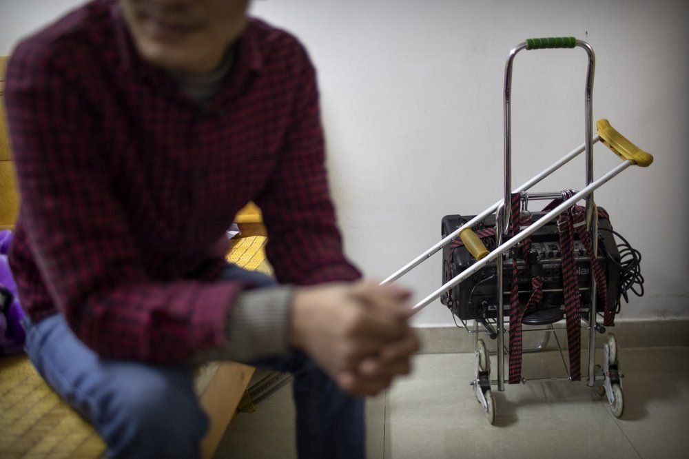 In this Dec. 5, 2019 photo, Wu Yi, who has struggled with Oxycontin abuse, sits in his rented room near his crutch and the portable amplifier he uses to sing songs for money in Shenzhen, southern China's Guangdong Province. Officially, pain pill abuse is an American problem, not a Chinese one. But people in China have fallen into opioid abuse the same way many Americans did, through a doctor's prescription. And despite China's strict regulations, online trafficking networks, which facilitated the spread of opioids in the U.S., also exist in China. Image by Mark Schiefelbein/ AP Photo. China, 2019.