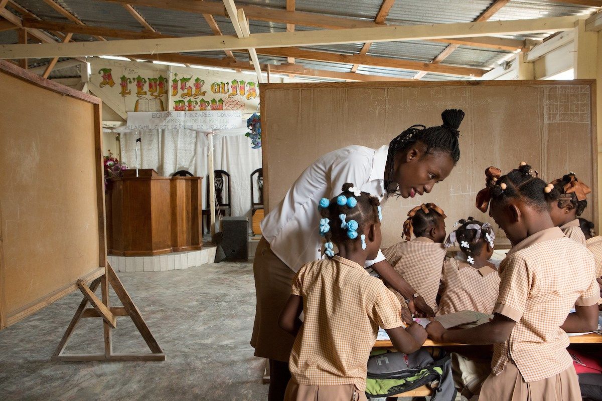 First grade teacher Andre Lydie works with her students on a lesson in the main sanctuary of the Church of the Nazarene, which doubles as an elementary school and is split into four classrooms during the week, in the Onaville section of Canaan. The church/school was founded by Pastor Marc Loumette in 2010. Seventy percent of the students are unable to pay their full school fees, but Loumette says he wouldn’t dream of kicking them out of school, though he has been unable to pay the teachers their salaries in four months. Image by Allison Shelley. Haiti, 2018.