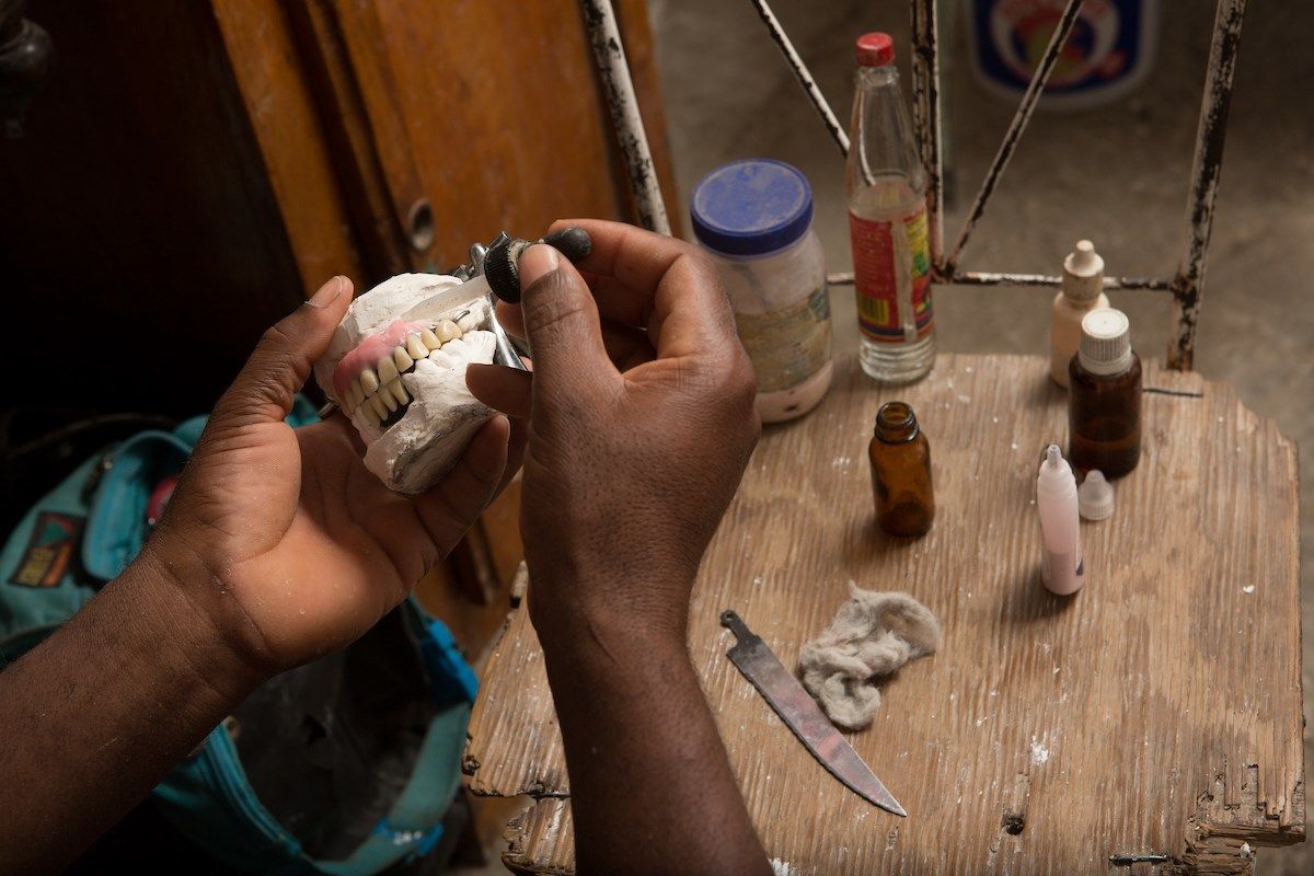 Sylphat Wilguive, 48, fabricates a set of dentures in his home in Jerusalem, just outside of Port-au-Prince. Sylphat had begun to construct a full dental clinic adjacent to his home when he was suddenly paralyzed, rendering him unable to work. The money that he had set aside over the years from the “Good Samaritan,” a clinic he once ran in the Delmas neighborhood, all went to pay for his medical treatment. He now does the work out of a room in his house, often treating needy neighbors for free. Image by Allison Shelley. Haiti, 2018.