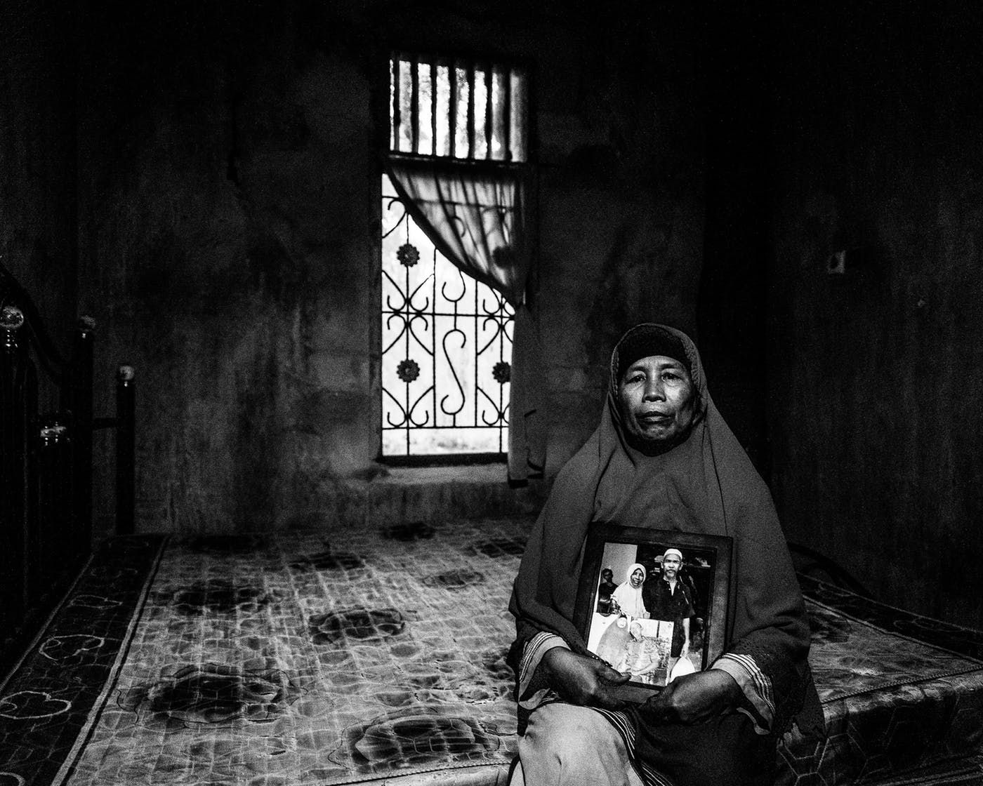 Kesuma Wati holds a photo of her and her husband, Bin Saimin, who was sent to jail for arguing with a plantation manager. Image by Xyza Cruz Bacani. Indonesia, 2018.