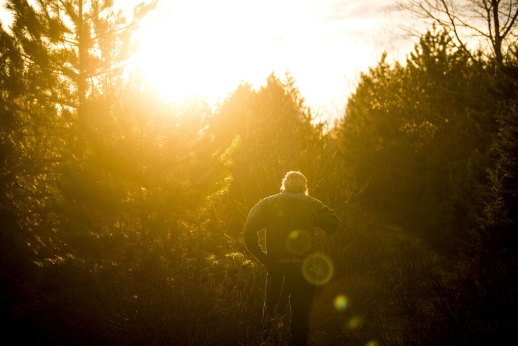 Duane Hanson walks in to the sunset near his homestead in the Unorganized Territories in the north woods of Maine near T5 R7 on May 6, 2019. Central Maine Power officials claim this area to be scarred by logging. Hanson points out that he is walking on an old logging road that has grown in. Image by Michael G. Seamans. United States, 2019.