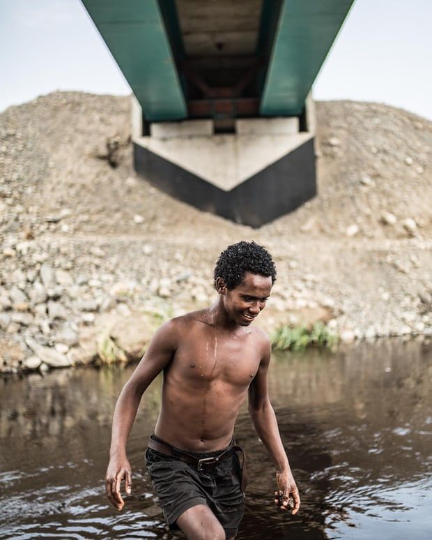 Ibrahim, 17, swims in the river beneath new tracks being built by a Turkish construction company in Awash National Park. Image by Charlie Rosser. Ethiopia, 2018.