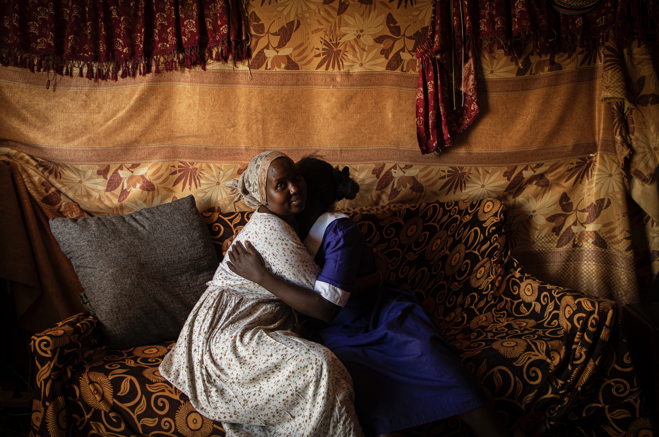 Dorcas Choya sits with Susie on her couch, who fled her home when her parents brought a circumciser to cut her. “When I saw her I just ran,” said Susie. “I didn’t bother taking anything. I ran without shoes." Image by Will Swanson. Kenya, 2020.