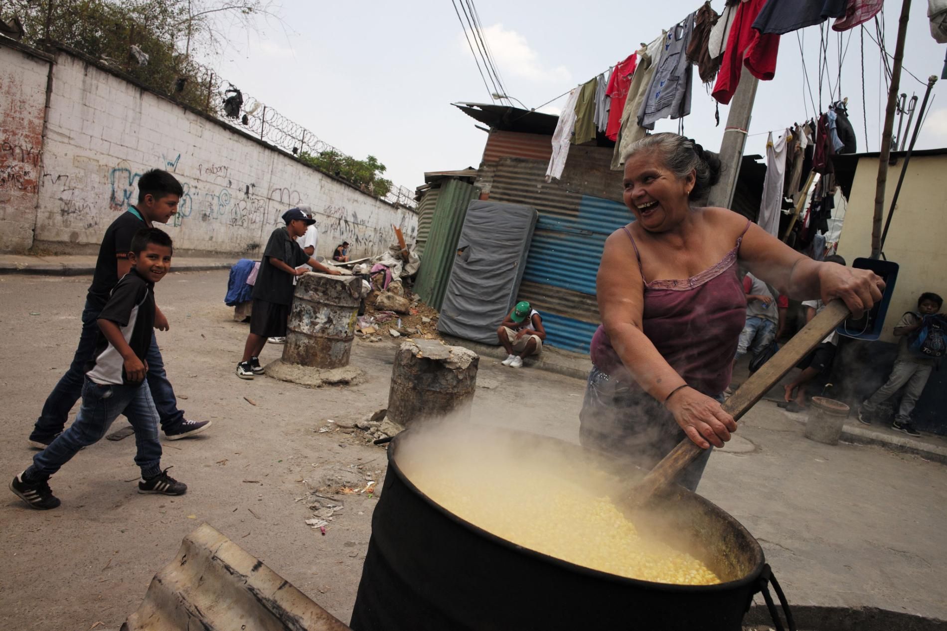 Alma Iris Garay, 50, who fled violence in El Salvador as a child, who has lost a son to drugs, beams as she stirs her vat of corn on a street corner, where the smoke from the open fire won’t choke her. She makes tortillas on a gas stove inside her home in Guatemala City. Image by Lynn Johnson. Guatemala, 2017.