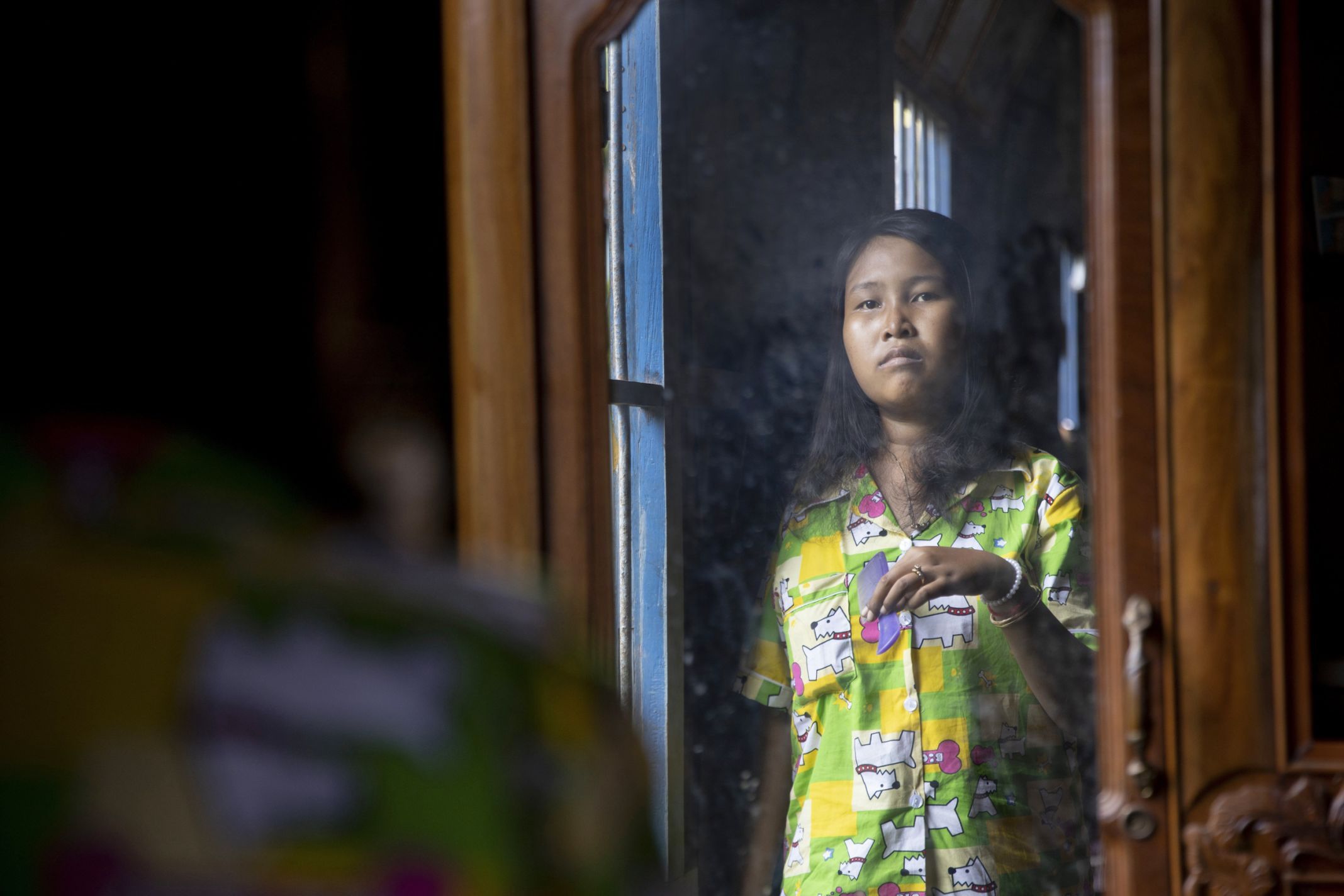 Lang Heang Khim, 22, looks in the mirror while brushing her hair in the village of Chong Trek. Image by Paula Bronstein. Cambodia, 2019.