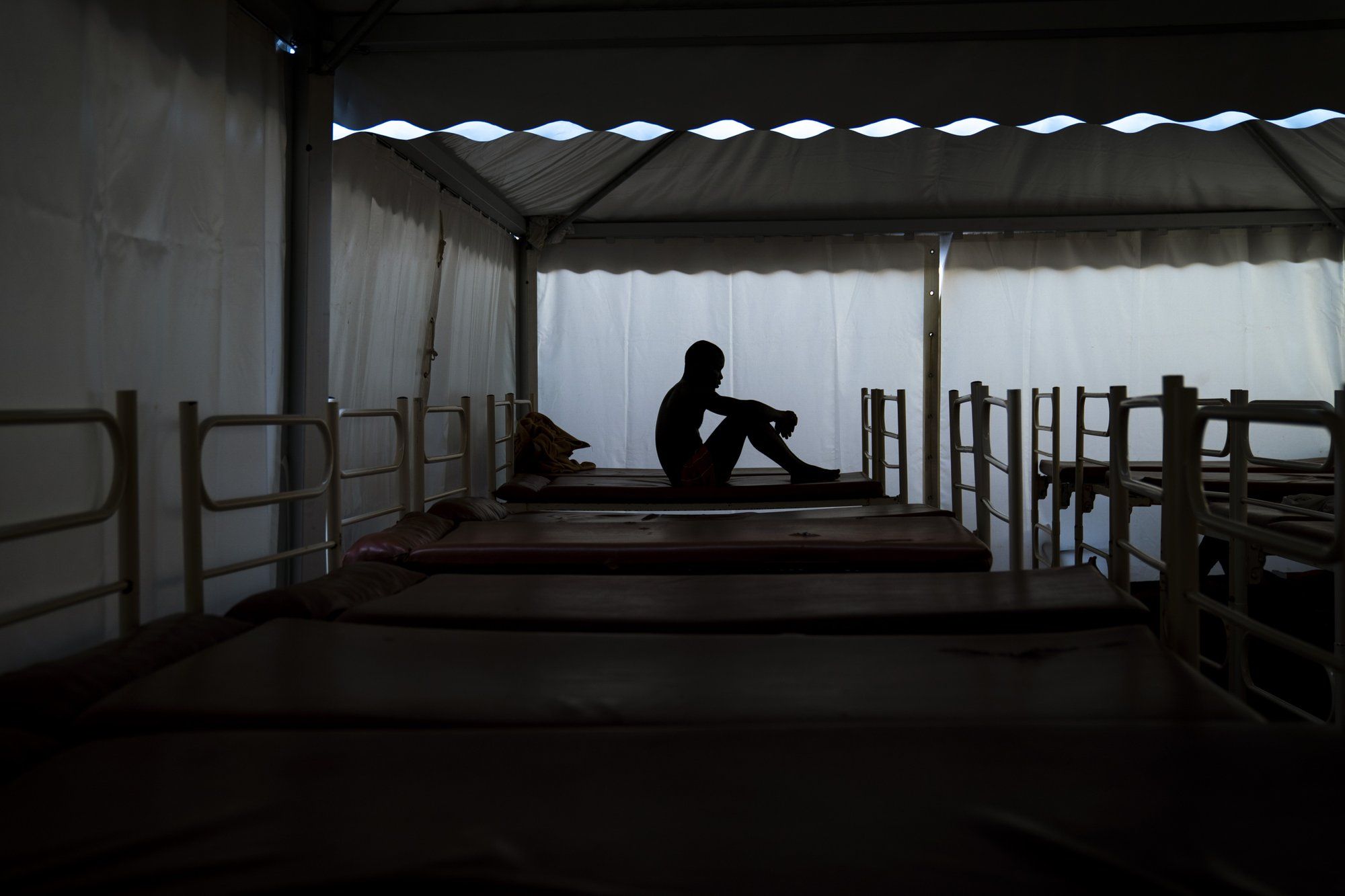 Mamadou Patherazi, from Guinea, sits on a bunk bed of the Modern Christian Mission Church in Fuerteventura, one of the Canary Islands, Spain, on Saturday, Aug. 22, 2020. Image by Emilio Morenatti/AP Photo. Spain, 2020.