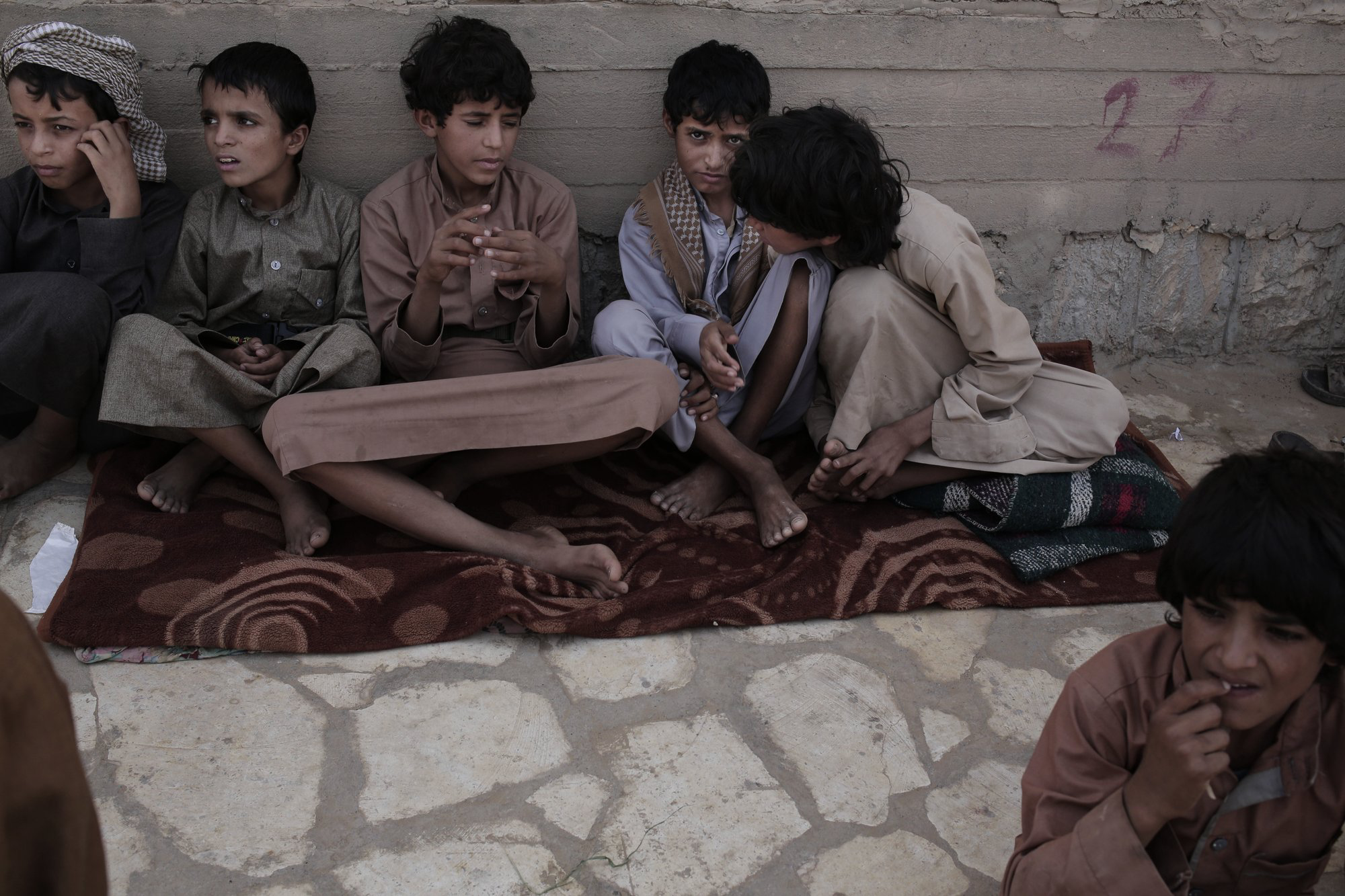 In this July 27, 2018 photo, 14-year-old Abdel Habid, second right, and 14-year-old Morsal, third right, sit at a camp for displaced persons where they took shelter in Marib, Yemen. Both boys were child soldiers forcibly enlisted by Houthi rebels and put to work carrying ammunition and supplies to the front lines. Abdel-Hamid says he saw children get shot for disobeying orders. Morsal suffered partial hearing loss from explosions and airstrikes. Image by Nariman El-Mofty / AP News. Yemen, 2018.