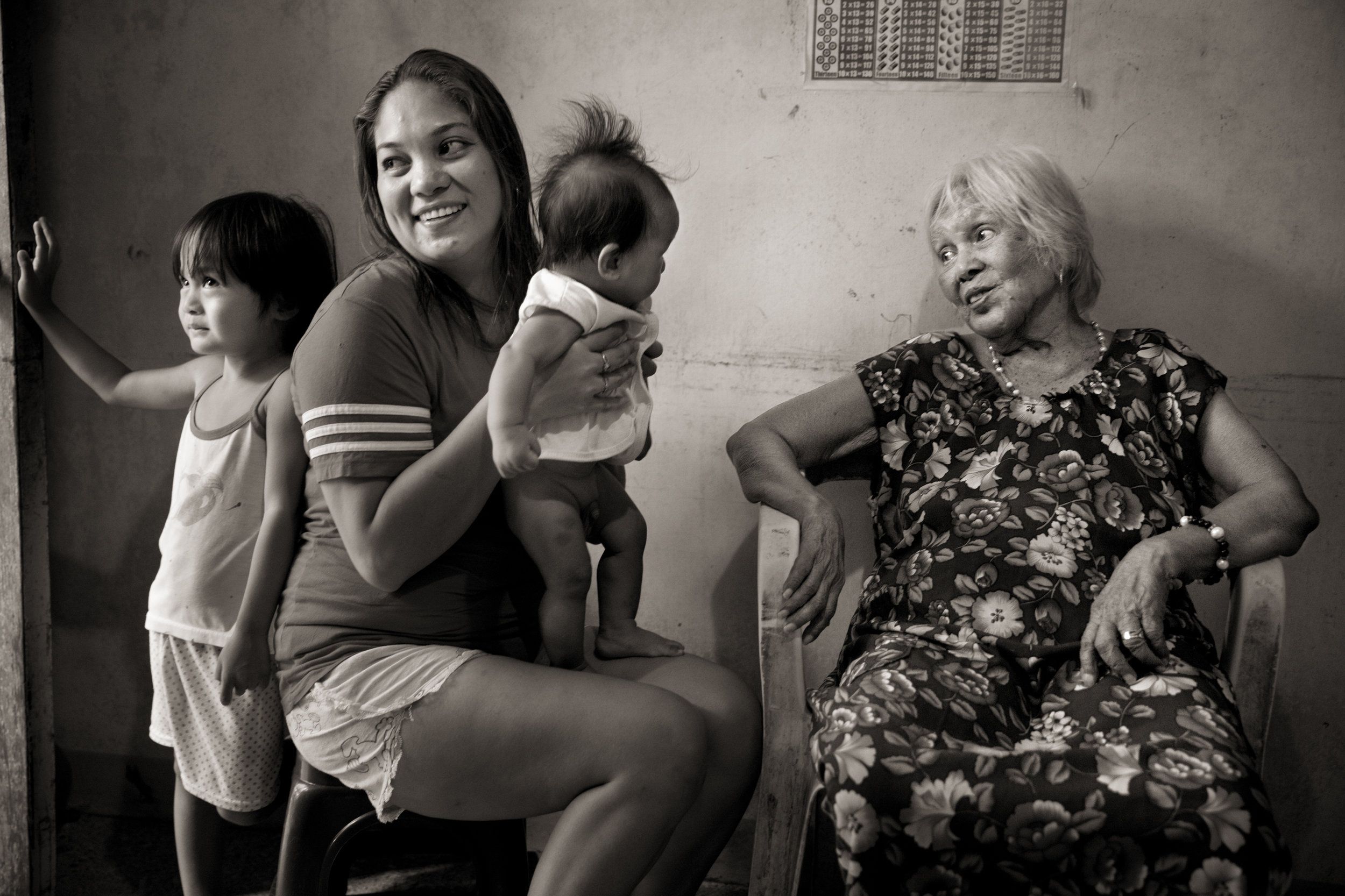 After singing for soldiers, Felicidad delos Reyes (right) was selected to "receive a gift" at the garrison behind her school. She was locked in a room; later five soldiers jumped on her, held her down and beat her into submission as they took turns raping her. Here, she is photographed with her great-granddaughter Lia Maglanit, great-grandson Elijah Maglanit and granddaughter Jonalyn Patiman. Image by Cheryl Diaz Meyer. Philippines, 2019.