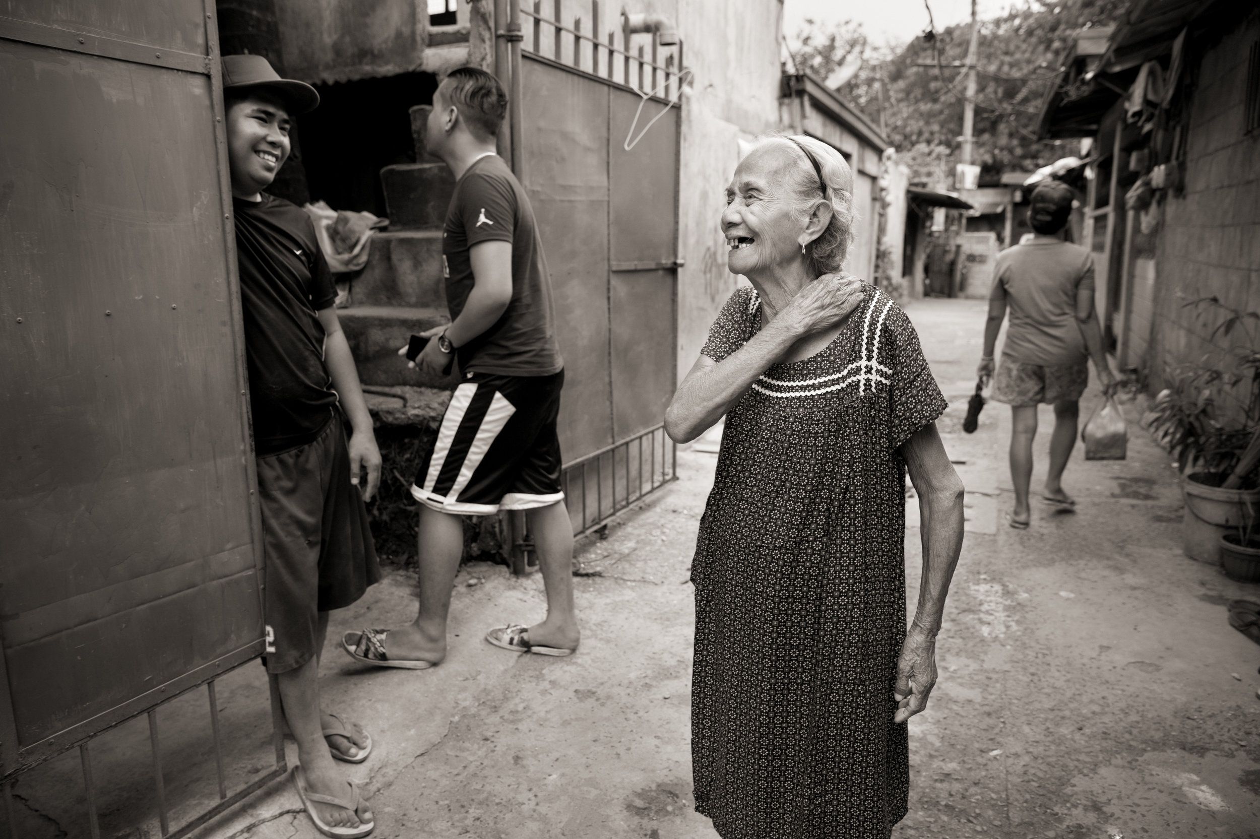 Narcisa Claveria laughs with neighbors in this 2019 photo. Even in the coronavirus pandemic, she goes out, wearing a mask. "I'd rather die in the streets," she says, "than stay dying of sadness at home." Image by Cheryl Diaz Meyer. Philippines, 2019.