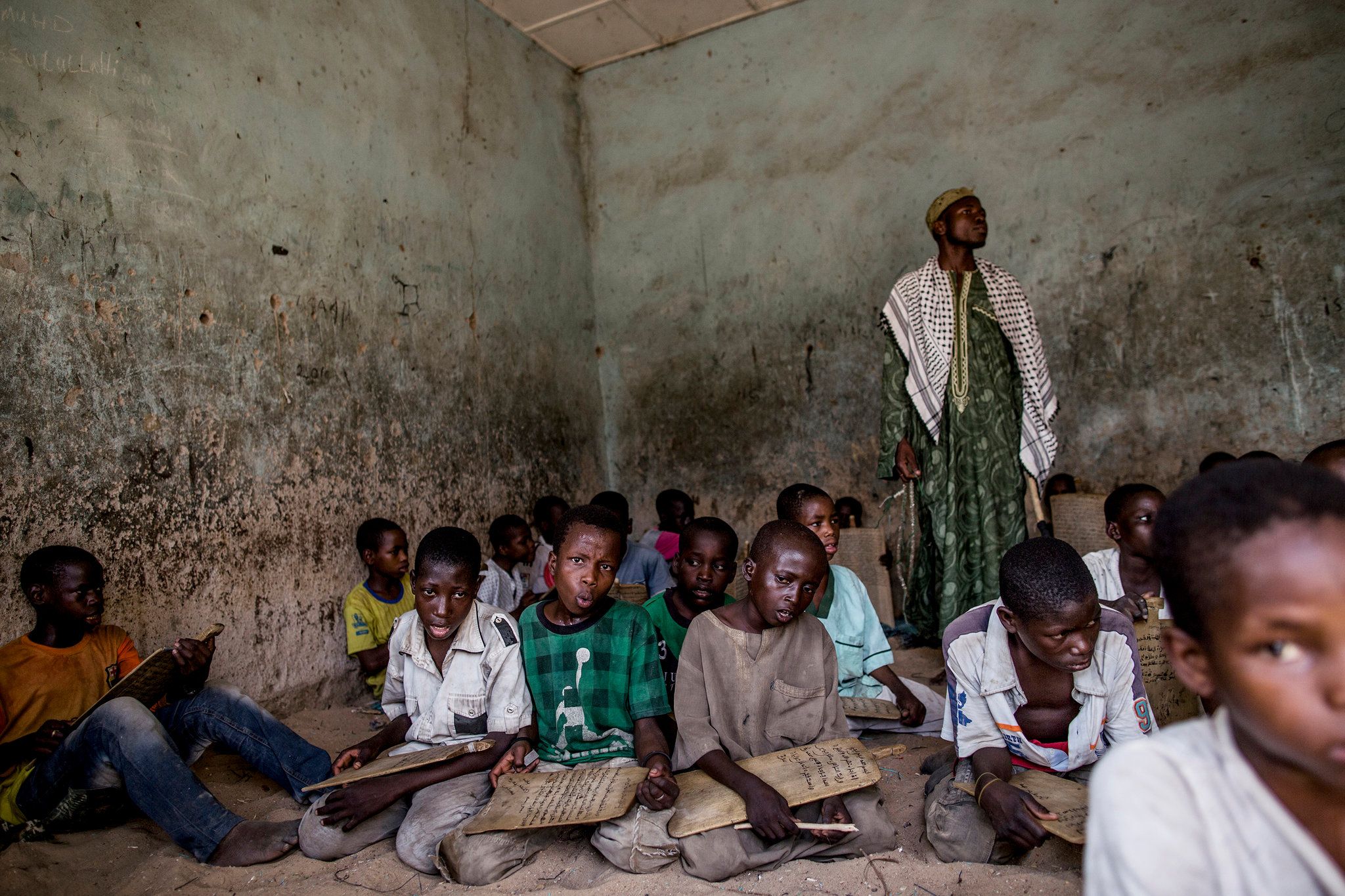 Young boys at an almajiri, a school for poor or orphaned children where they study the Quran and often must beg on the streets to cover their upkeep. Mallam Idris Muhammad, standing, is their teacher. Image by Glenna Gordon. Nigeria, 2017.