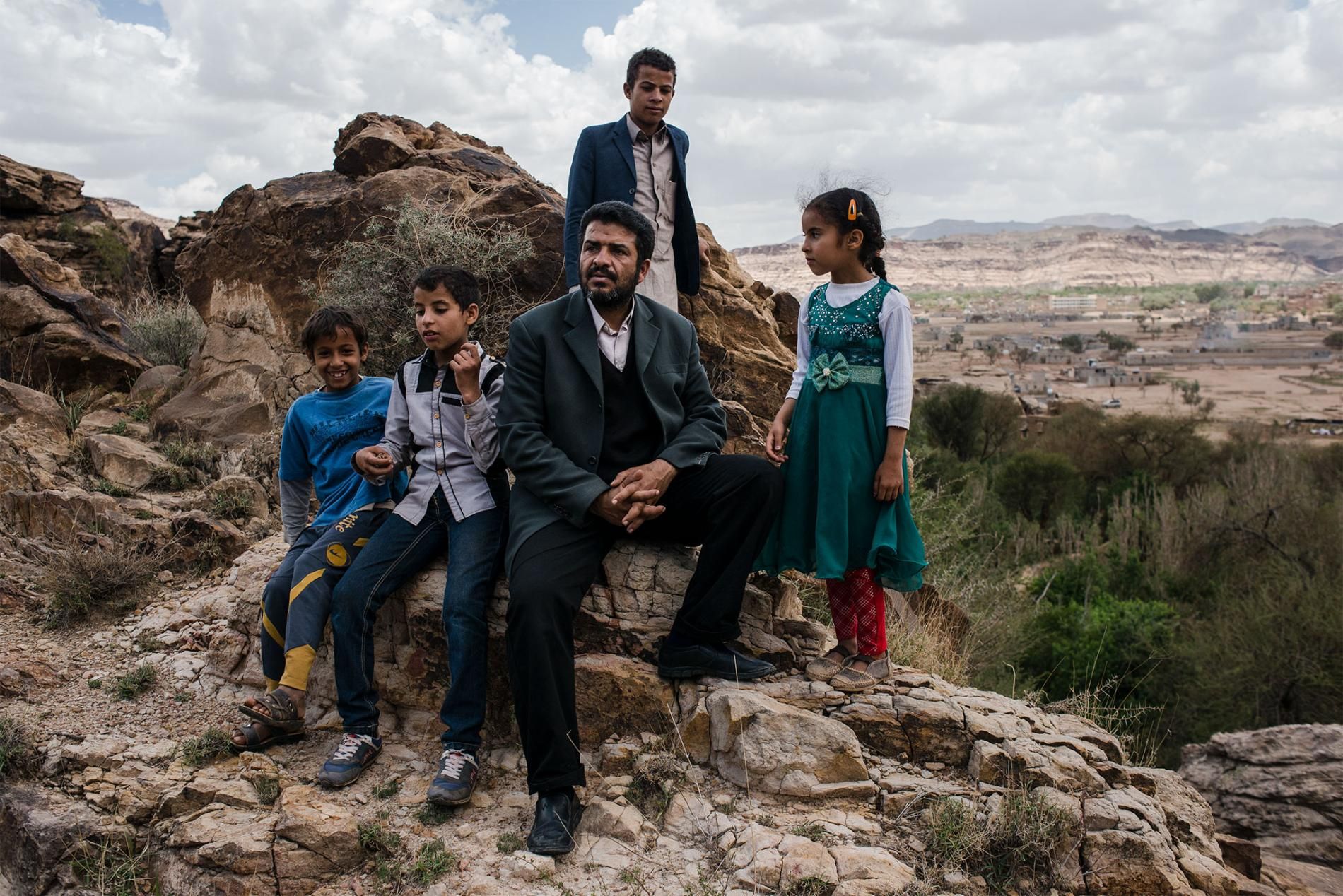 Yahya Abdullah sits with local children near a rocky trail in Wadi Dhahr. Image by Alex Potter. Yemen, 2018.