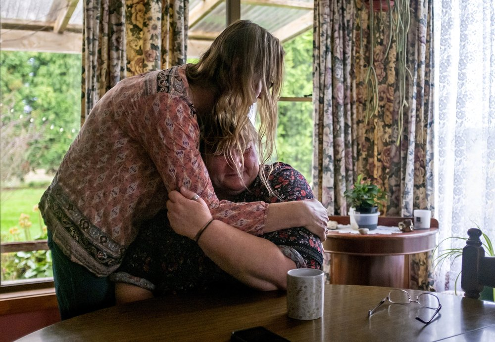 Carmall Casey, right, is embraced by Maxine Piper, a longtime friend and a source of support through Casey's addiction to opioids and battle with chronic pain, at her home in Black River, Tasmania, Australia, Tuesday, July 23, 2019. Casey doesn't know what she'll do when the pain returns. But she says she will never return to opioids. "I'm not going back," she says and begins to weep. "I'm not." Image by David Goldman. Australia, 2019.
