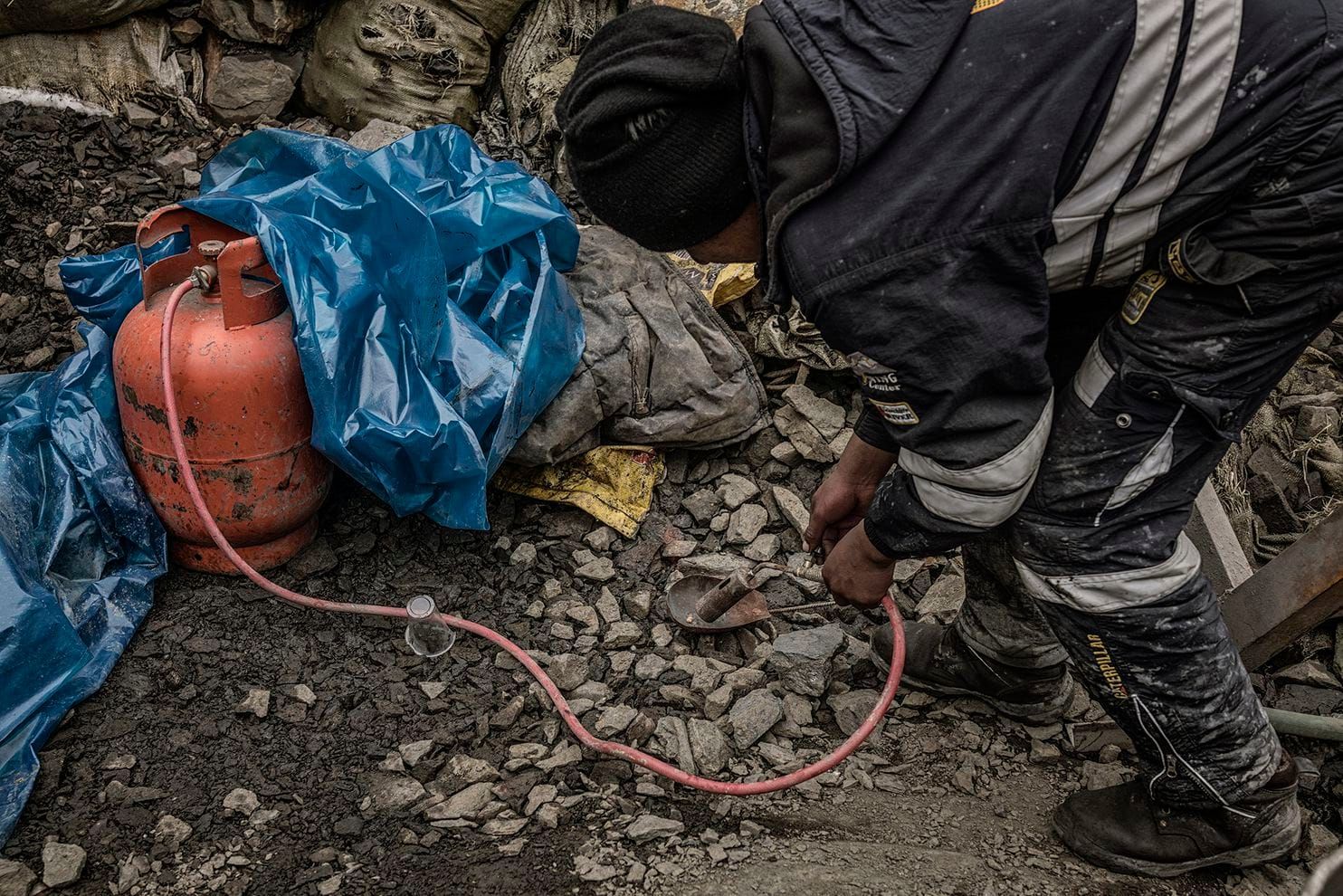 A worker laboring without any protection uses a blow torch with a flame so hot that it is invisible. It vaporizes mercury used to isolate gold from ore. Peru, 2019. Image by James Whitlow Delano.