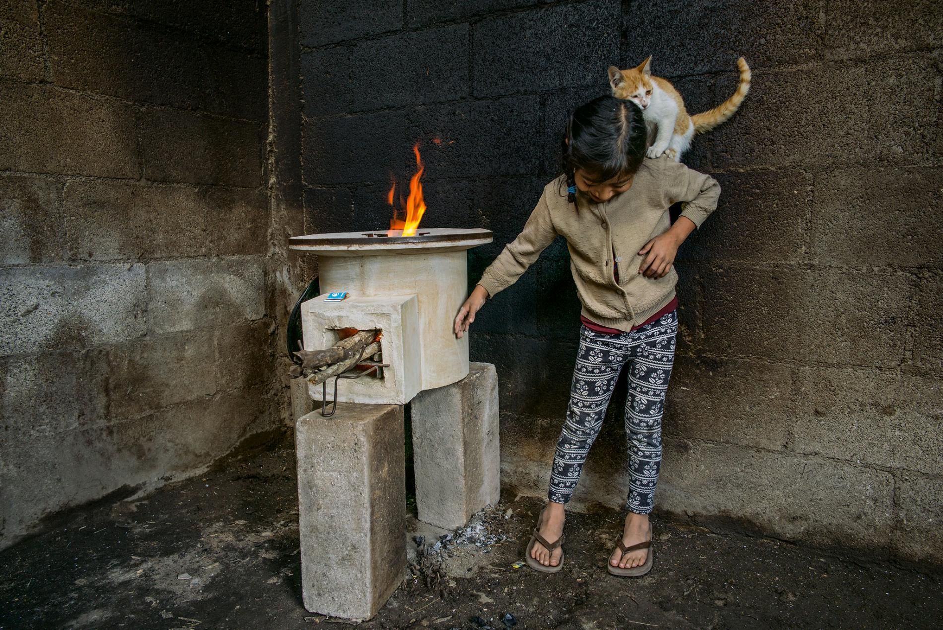 Tania López, seven, plays with her cat in a room whose walls were blackened by an old open fire; the new stove, provided by StoveTeam International, is efficient and safe to touch. Image by Lynn Johnson. Guatemala, 2017.