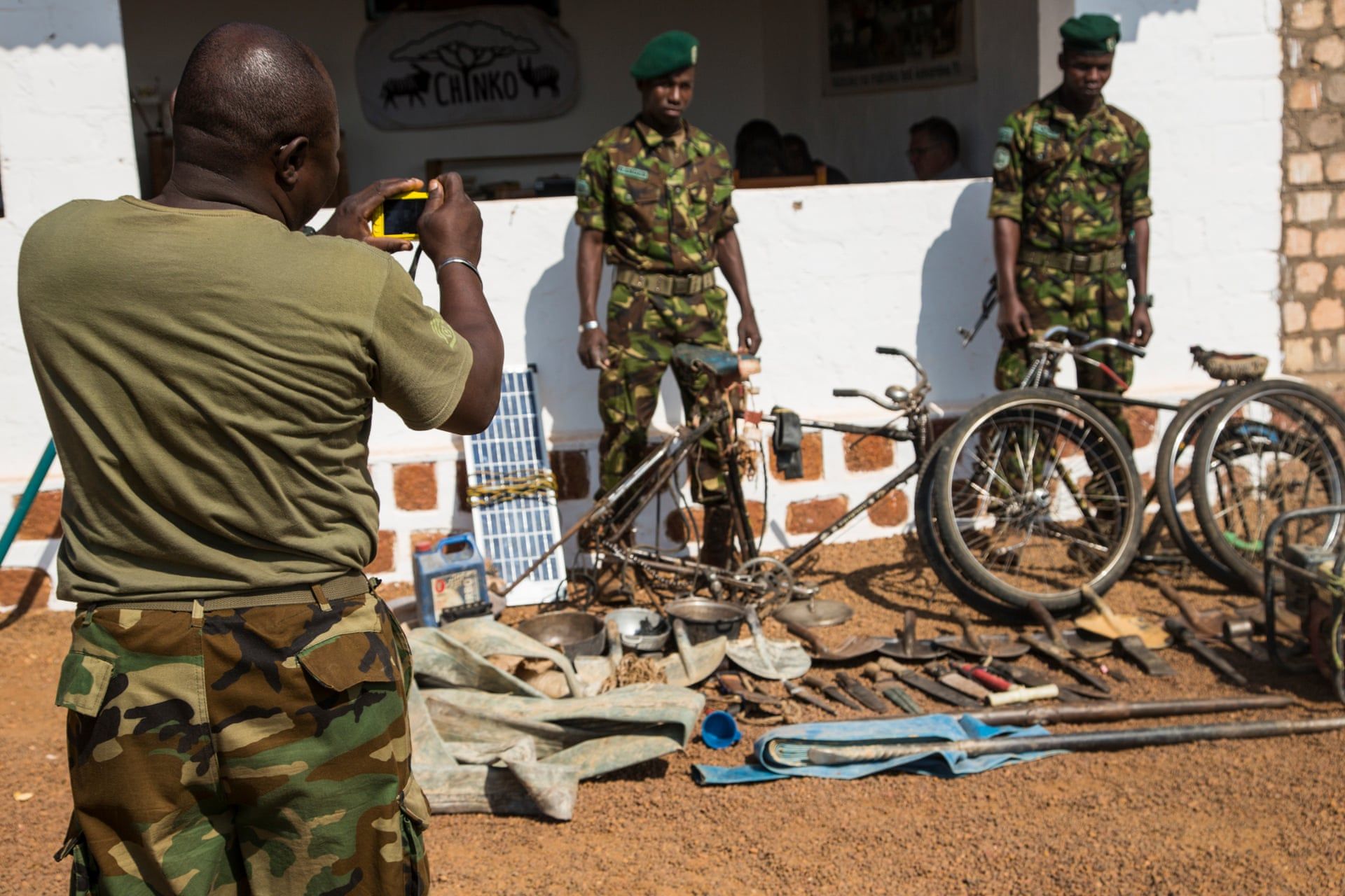 Two rangers pose for a photo next to machetes, knives, spades and other equipment which have been confiscated from poachers and laid out at Chinko’s HQ. Image by Jack Losh. Central African Republic, 2018.