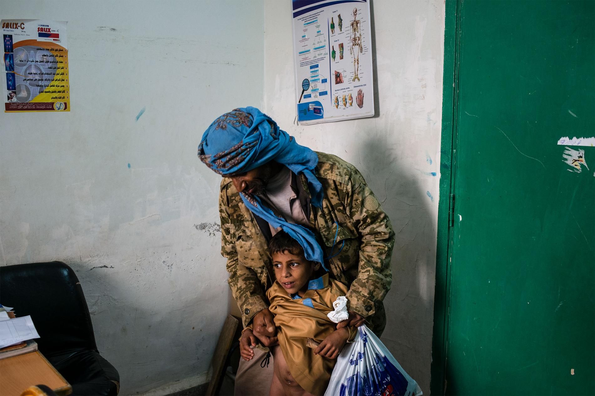 Rasheed al Suwaidy shows a urologist the fistula on the stomach of his son, Mohammad. The condition causes Mohammad to have trouble urinating, often soiling his clothing, and Rasheed can't afford the surgery necessary to fix it. Image by Alex Potter. Yemen, 2018.