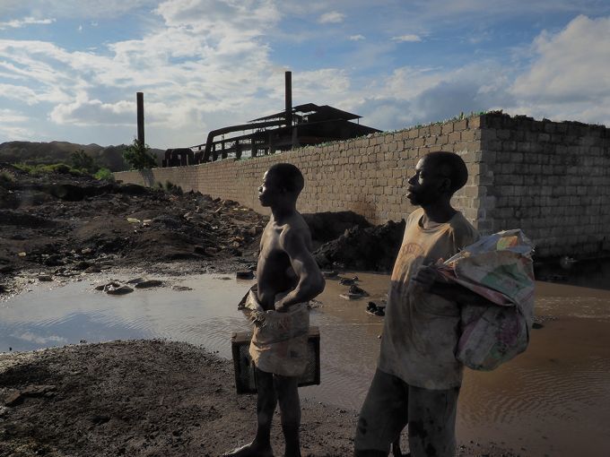 Miners stand in front of a Chinese smelter that reprocesses slag from the area. The smelter produces manganese and spews dense plumes of toxic smoke over the Kabwe area. Image by Larry C. Price. Zambia, 2017.