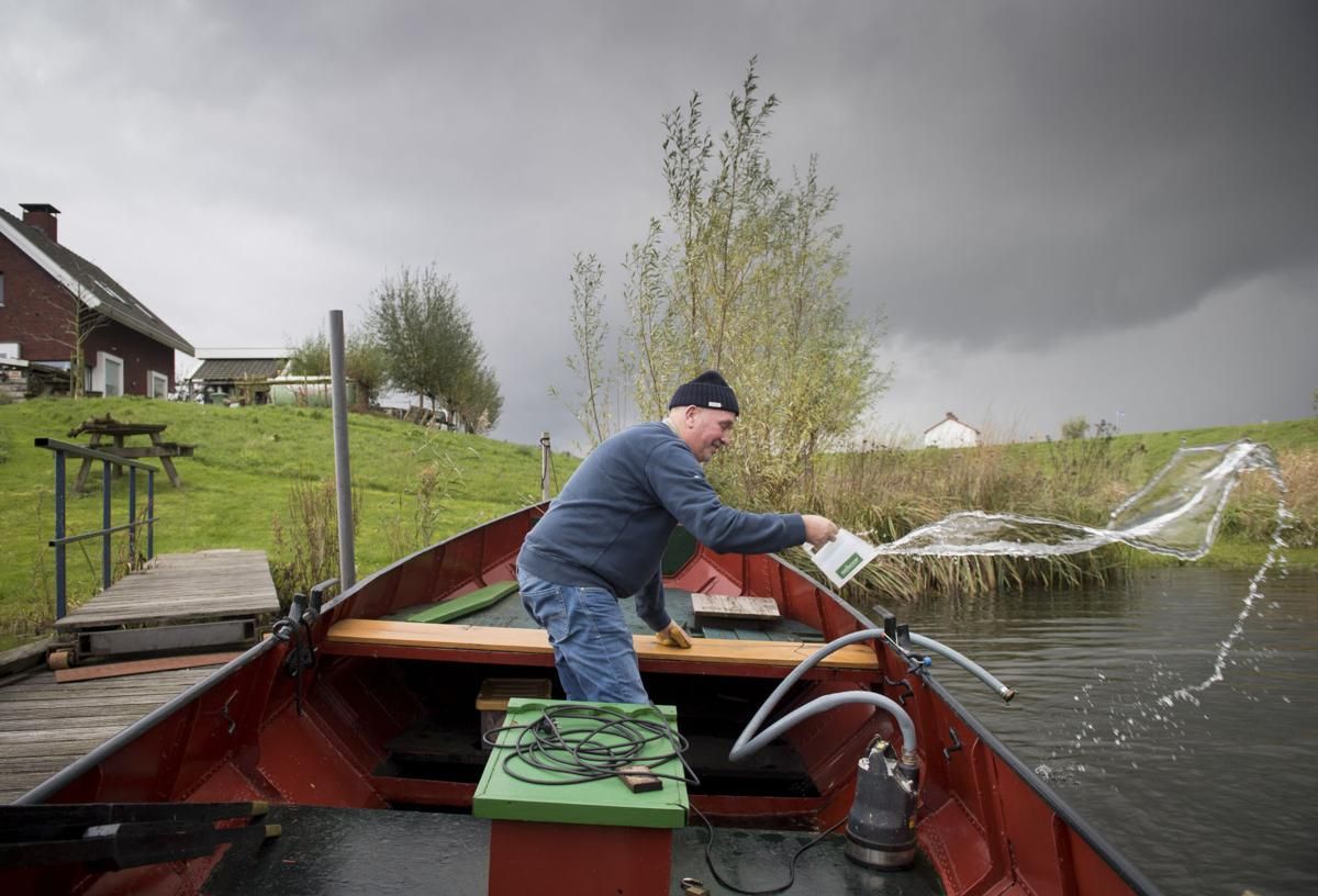 Vic Gremmer bails out his wooden boat before a rain storm in South Holland. Gremmer agreed to relocate his home as part of a program that makes room for for rivers to flood safely. Image by Chris Granger. Netherlands, 2019.
