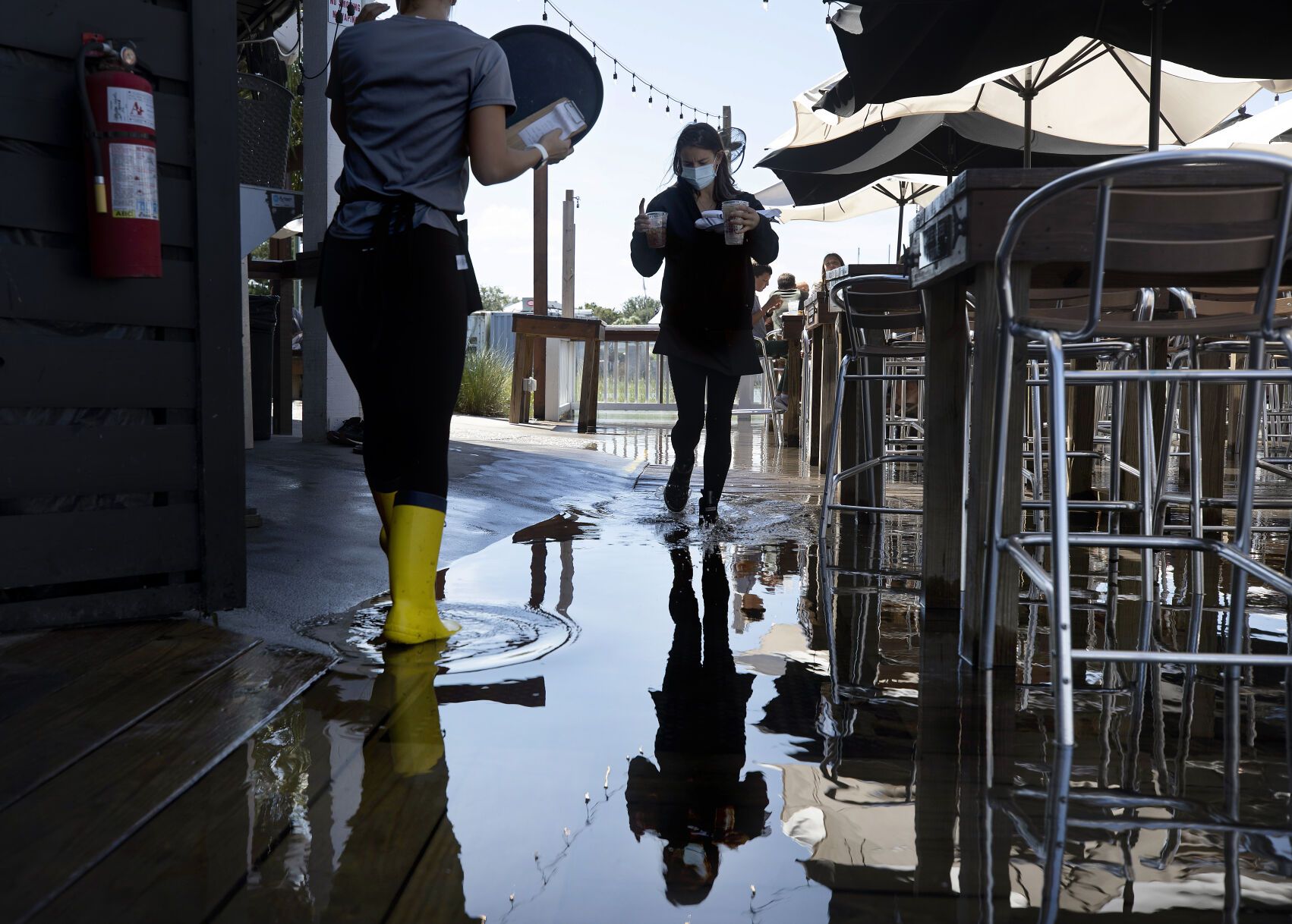 Servers Alexandra Schroettner and Christi Hughes wade through salt water that has risen over the patio at Saltwater Cowboys as they serve guests lunch on Shem Creek on Monday, Sept. 21, 2020, in Mount Pleasant. Image by Grace Beahm Alford / Post and Courier. United States, 2020.