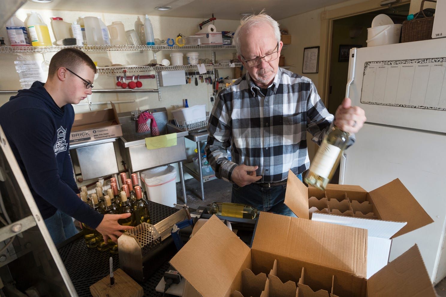 Tom Rohland fillls cases of wine with the help of Isaac Mathison, left, at the Munson Bridge Winery in Withee. Image by Mark Hoffman. United States, 2019.