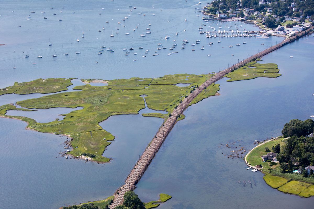 The Northeast Corridor Line, a 735-kilometer stretch of rail line, often follows the shoreline, such as here, near Groton, Connecticut. Soon the route could be beset by episodes of submersion that would erode the trackbed and disable signaling equipment, disrupting travel for the approximately 12 million passengers who rely on it each year. A recent study of a 16-kilometer segment owned by Amtrak near Wilmington, Delaware, proposed a $78-million package of flood barriers that could be erected during storms. Image by Alex MacLean. United States, 2019.