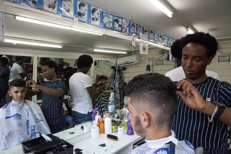 In this Wednesday, Aug. 8, 2018 photo, Eritrean migrant Gharmay Negassi works at a barbershop in Tel Aviv, Israel. African migrants coming into Israel have been detained, threatened with deportation, and faced hostility from lawmakers and residents. Now, they face another burden: a de facto 20 percent salary cut that has squeezed them financially and driven them further into poverty. Image by Caron Creighton. Israel, 2017.
