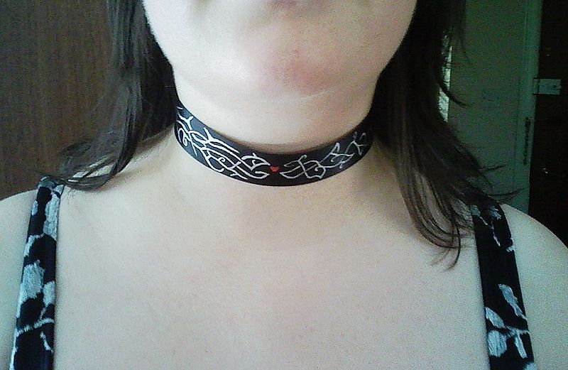 A woman wears a black choker with white designs on it.
