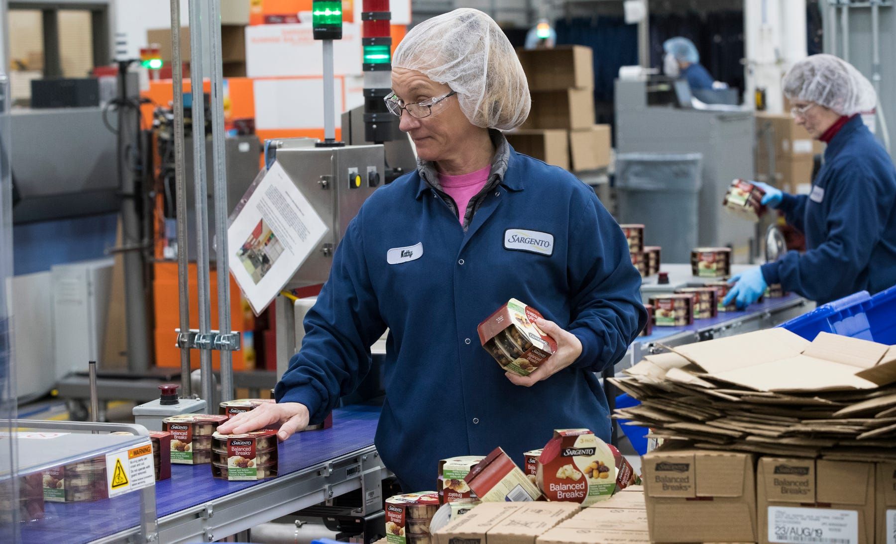 Kathy Griffey, top, and Kristin Geary, bottom right, work on an assembly line packaging Balanced Breaks snacks at Sargento Foods Inc. The company employs about 2,300 people in Wisconsin. Image Courtesy of Mark Hoffman. United States, 2019.