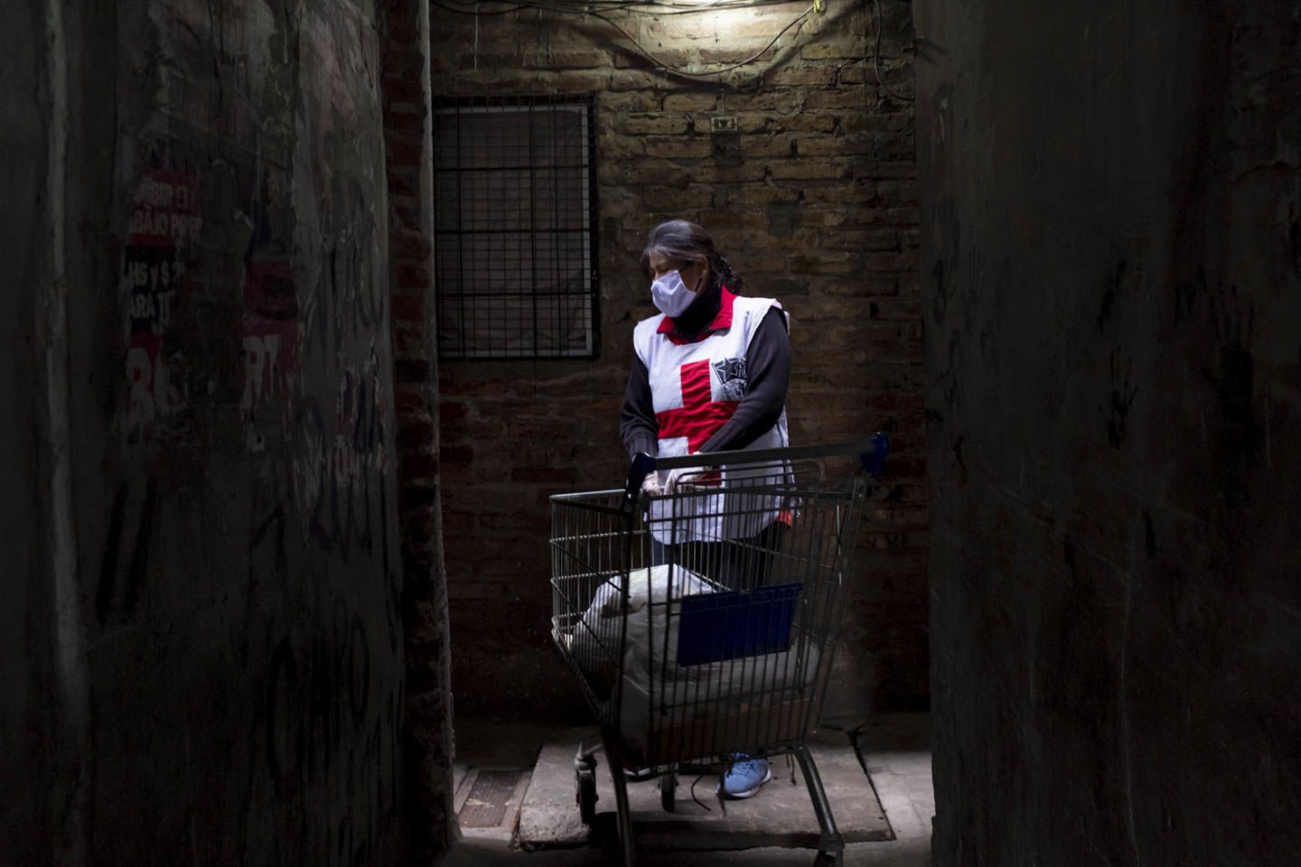Yoli, in one of the dark and narrow corridors of the Villa, delivering supplies to those homebound. Image by Anita Pouchard Serra. Argentina, 2020.