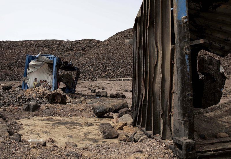 Mohammed Eisa, a 35-year-old Ethiopian farmer, and other migrants he met along the way, take shelter inside a damaged shipping container on the side of a highway, near Lac Assal Djibouti, July 14, 2019. Many migrants have made the journey to Saudia Arabia multiples in what has become an unending loop of arrivals and deportations. Eissa is among them; this is his third trip to Saudi Arabia. Image by AP Photo / Nariman El-Mofty. Djibouti, 2019.