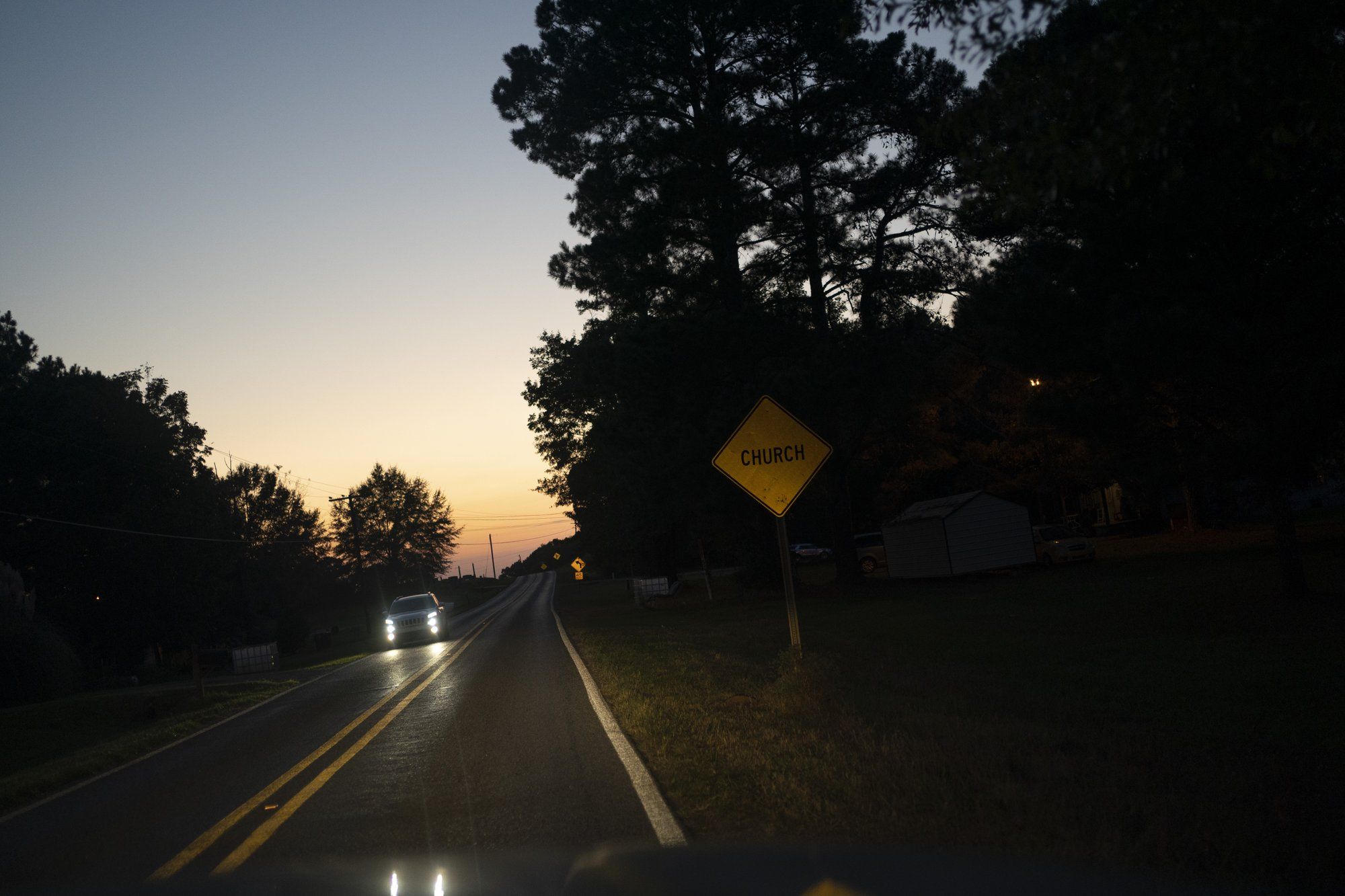 A vehicle travels down a road along Mt. Zion United Methodist Church at dusk in Philadelphia, Miss. Image by Wong Maye-E / The Associated Press. United States, 2020.