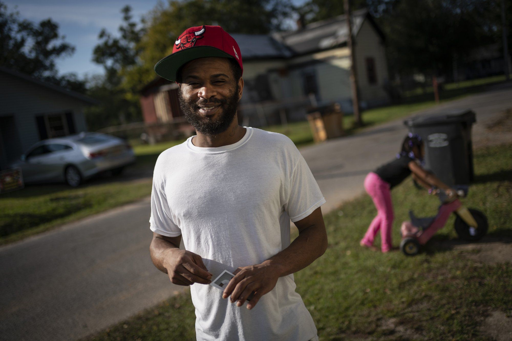 Demarkio Pritchett, 29, stands with his daughter Mariah Pritchett, 8, playing in the background outside his grandmother's home in Meridian, Miss. Image by Wong Maye-E / The Associated Press. United States, 2020.
