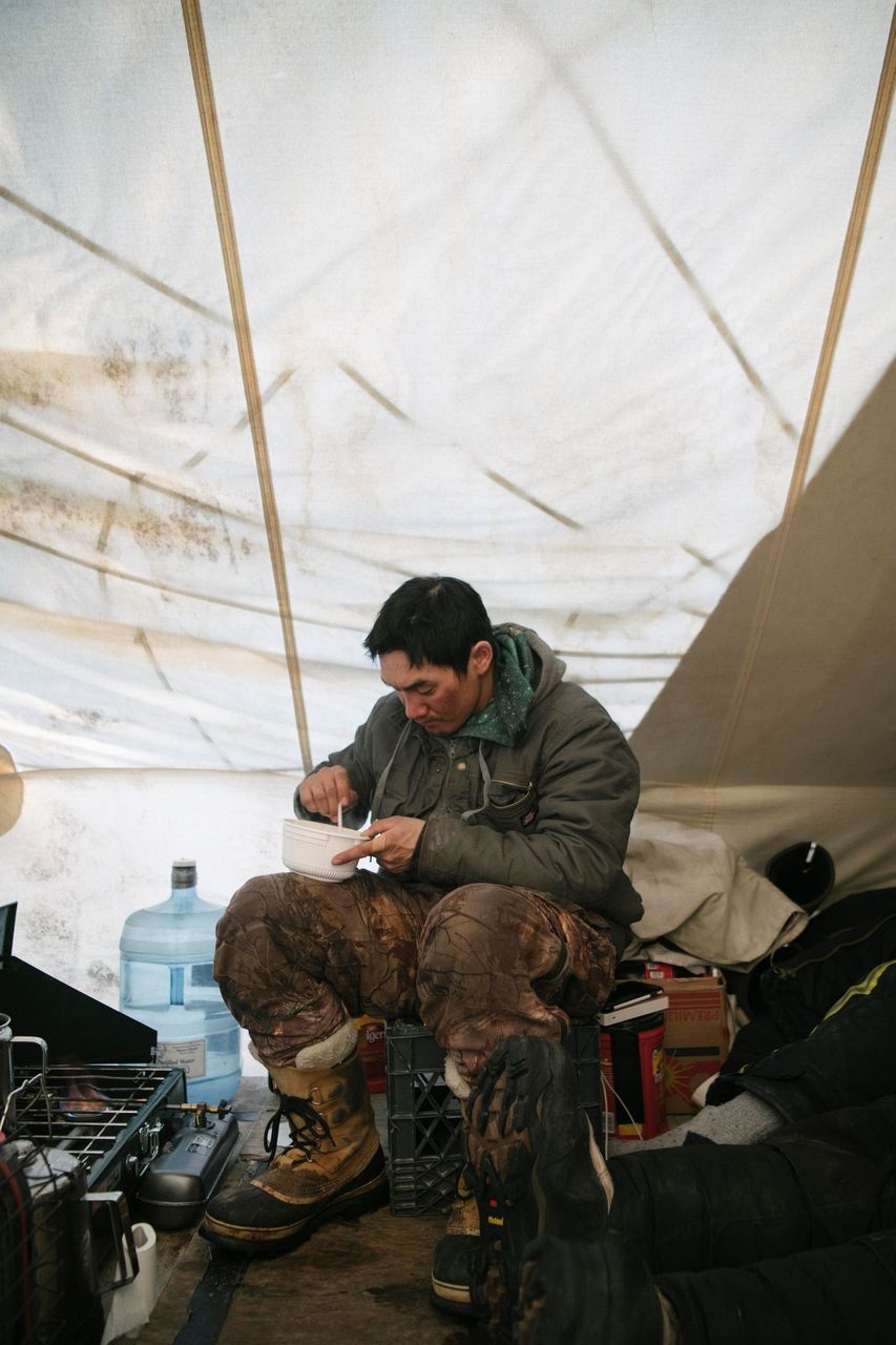 JR Nungasak scrapes a bowl clean inside a whaling camp tent as he takes a break from the perpetual watch of whaling. Image by Kiliii Yuyan. United States, undated.