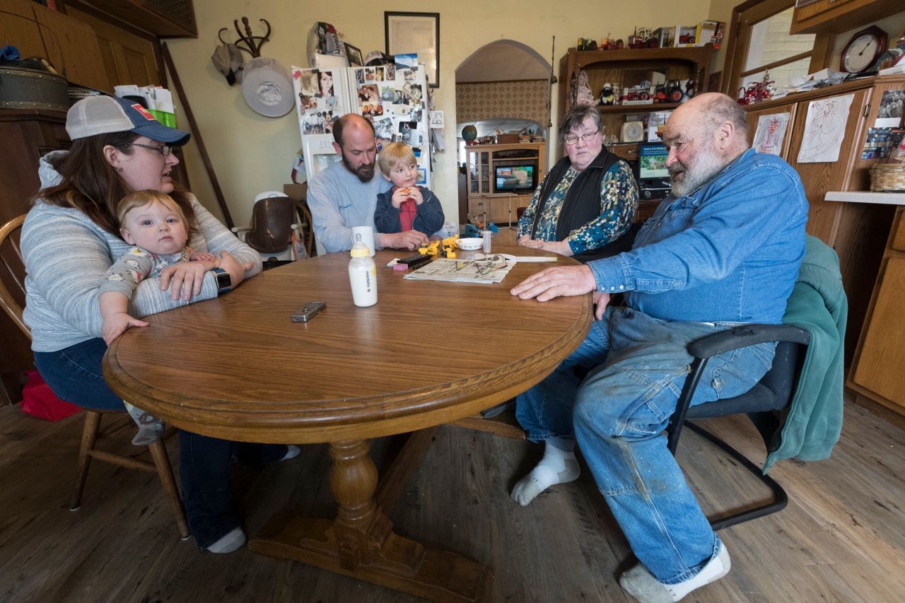 The Mess family, Carrie Mess, from left, with her 10-month-old son, Ben; husband, Patrick, with 3-year-old son Silas; and Cathy and Clem Mess, gather around their kitchen table on their farm in Watertown. Image by Mark Hoffman. United States, 2019.