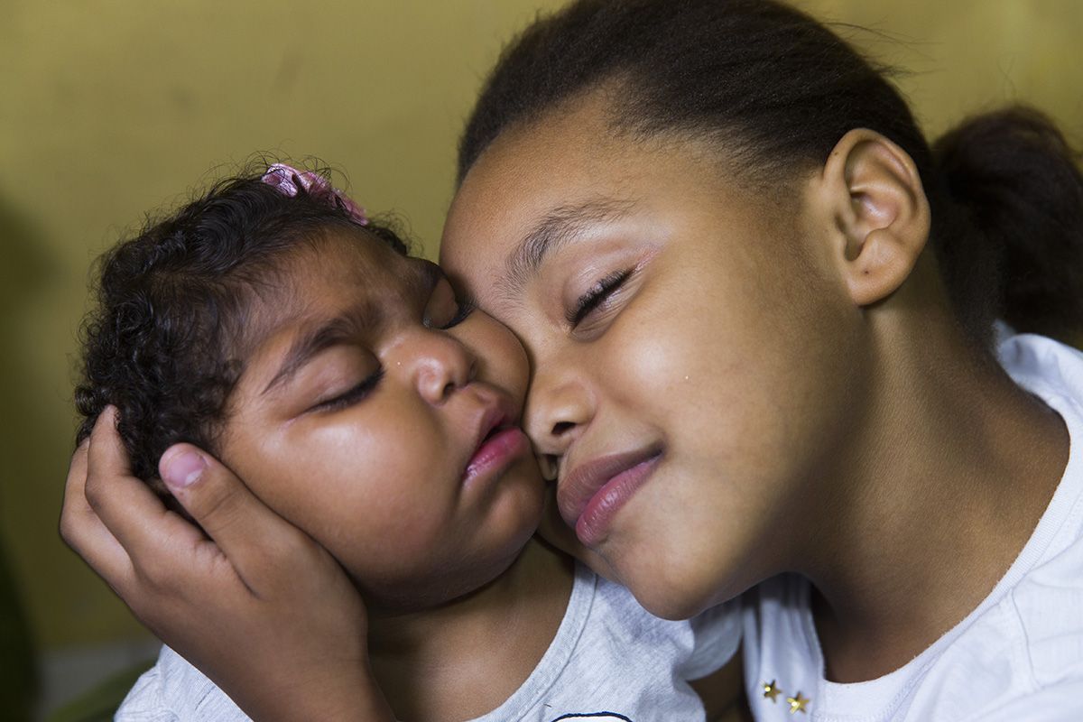 Fabiane Lopes gets medicine for her daughter, Valentina, at their home (left) in Duque de Caxias, a suburb of Rio de Janeiro in southeastern Brazil, while Eduarda Lopes, 9, holds her sister (right). Image by Mark Hoffman. Brazil, 2017.