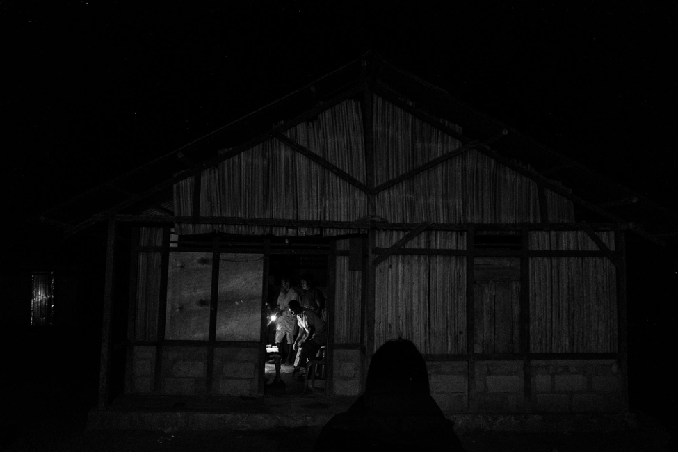 Members of Adelina’s family gather at their home in Ponu, which, like many neighboring villages, has no access to electricity. Though these communities have played the smallest role in causing global warming, they are the hardest hit by it. With the climate changing, millions more people like Adelina and Dolfina will be forced into migration for survival. And unless regulations and enforcement improve — both in the countries people flee, and the ones in which they settle — cases like these will grow tragically ever more common. Image by Xyza Cruz Bacani. Indonesia, undated.