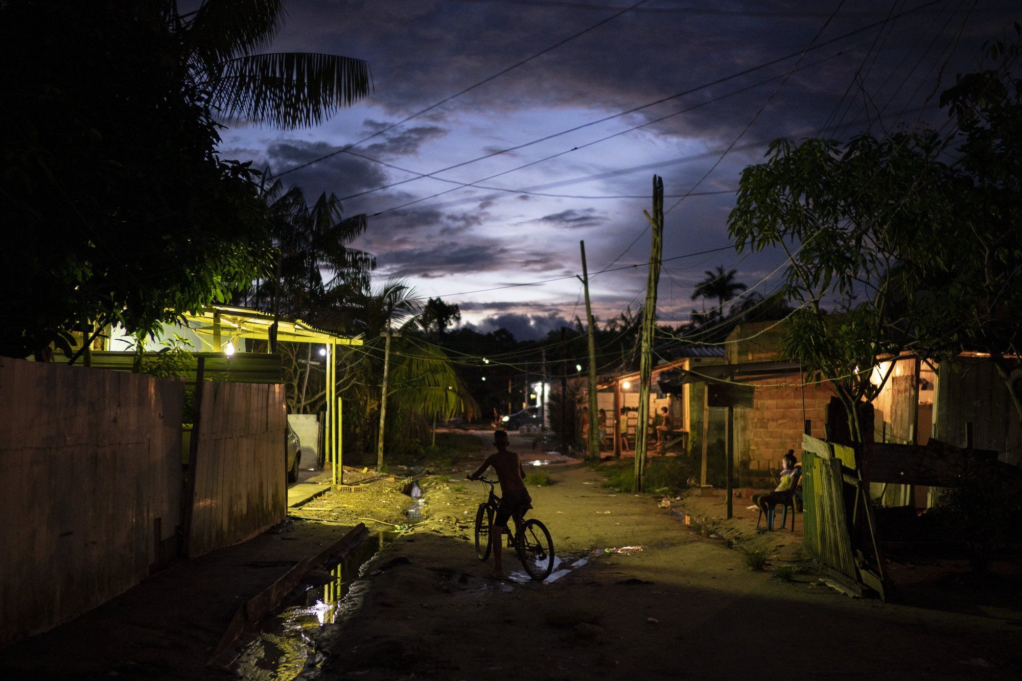 A boy rides his bike at dusk through the Park of Indigenous Nations community, where many residents have fallen ill with symptoms of the new coronavirus, in Manaus, Brazil, Sunday, May 10, 2020. Image by Felipe Dana. Brazil, 2020.