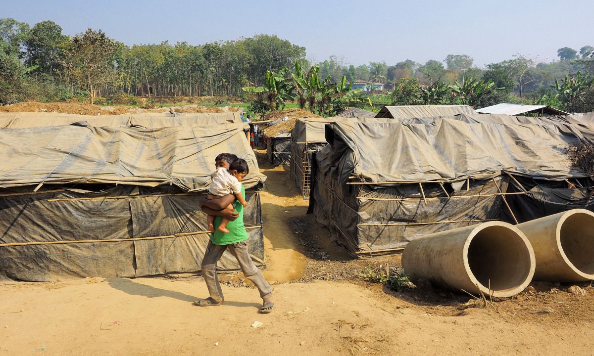 A boy carries another child in Kutapalong Refugee Camp. In this unofficial camp, tents are constructed with plastic tarps that had been used to evaporate seawater. Image by Doug Bock Clark. Bangladesh, 2017.