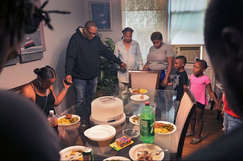 Cecil Burton – viewed as a "deadbeat dad" by many for his child support debt – leads his family in prayer: "Father God, thank you for showing my family what true love is. Let’s eat and have fun and enjoy ourselves." At 54, much of the debt he owes is to the state to repay welfare benefits his children received when they were young. Image by Karl Merton Ferron / Baltimore Sun. United States, 2019. 