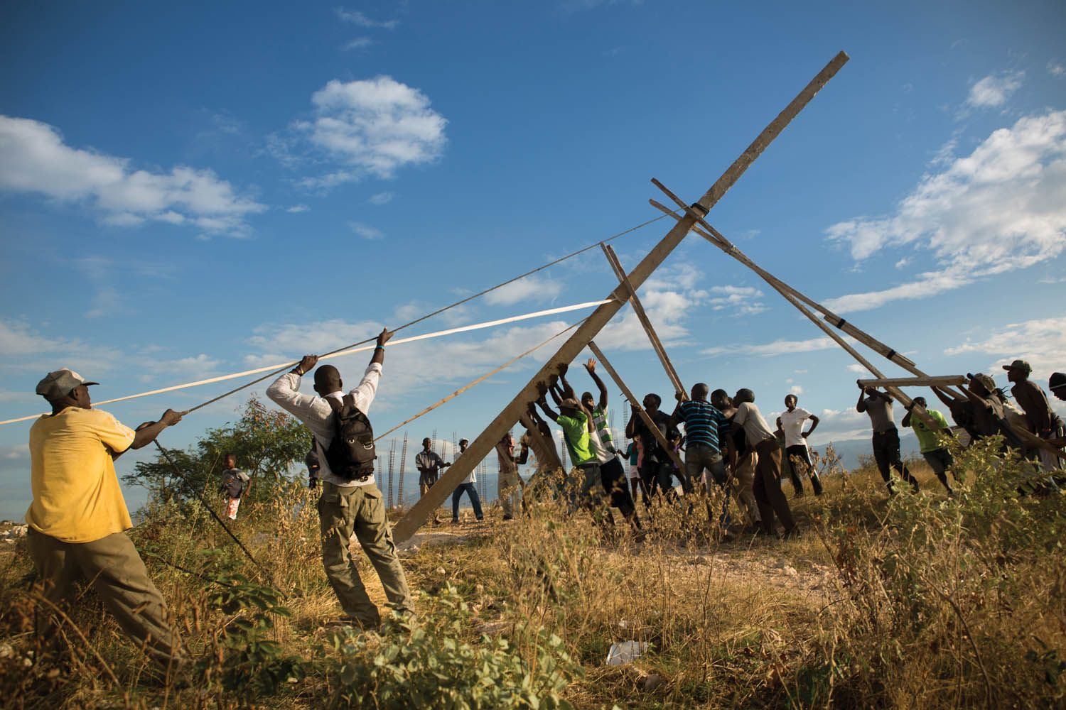 Residents of Canaan raise the first of three handmade utility poles, part of an improvised effort to receive electricity from the state power grid. Image by Allison Shelley. Haiti, 2017.
