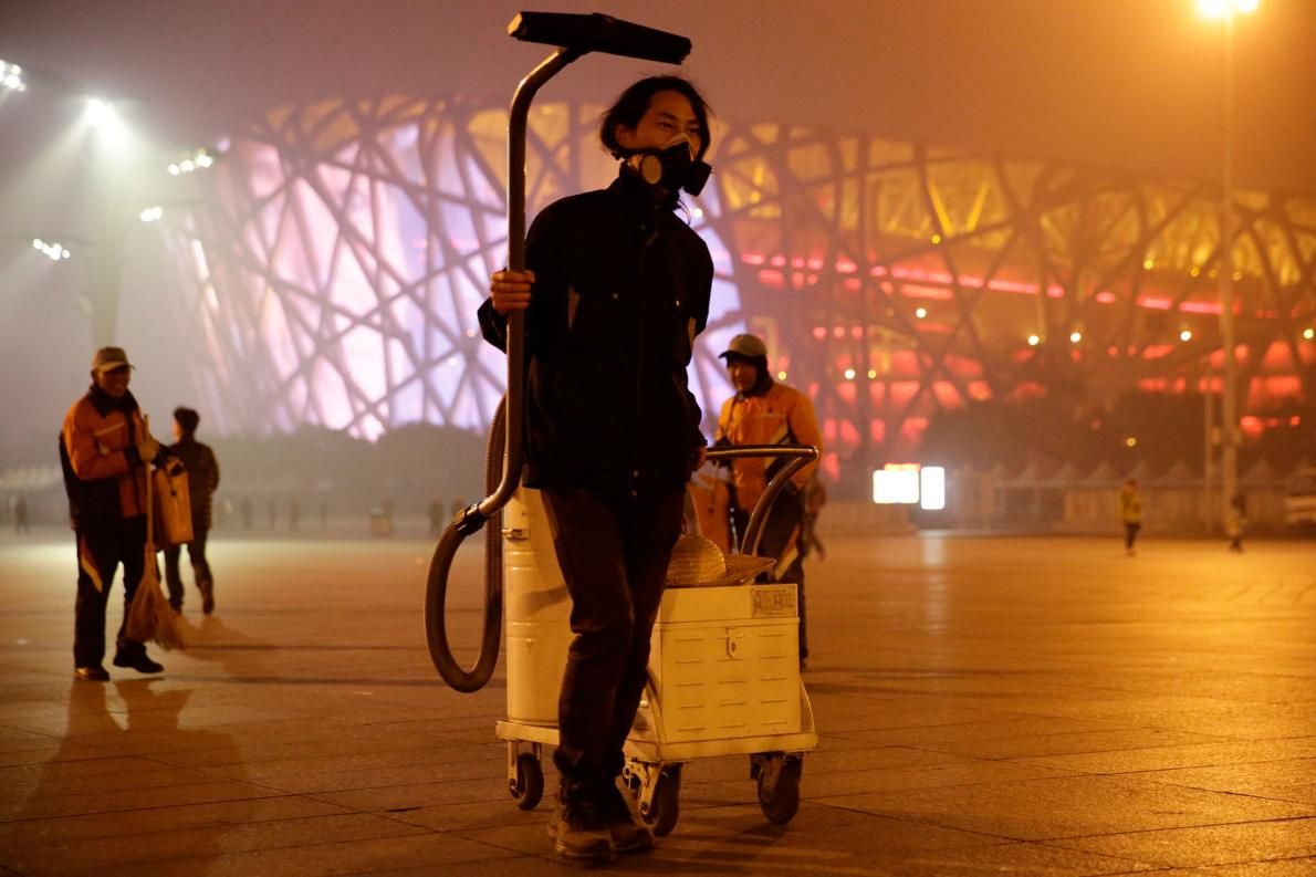 "Brother Nut" collects smog with an industrial vacuum cleaner near the Bird's Nest stadium in Beijing, in November 2015. He later made the dust into a brick. Image by Dong Dalu, VCG. China, 2015.