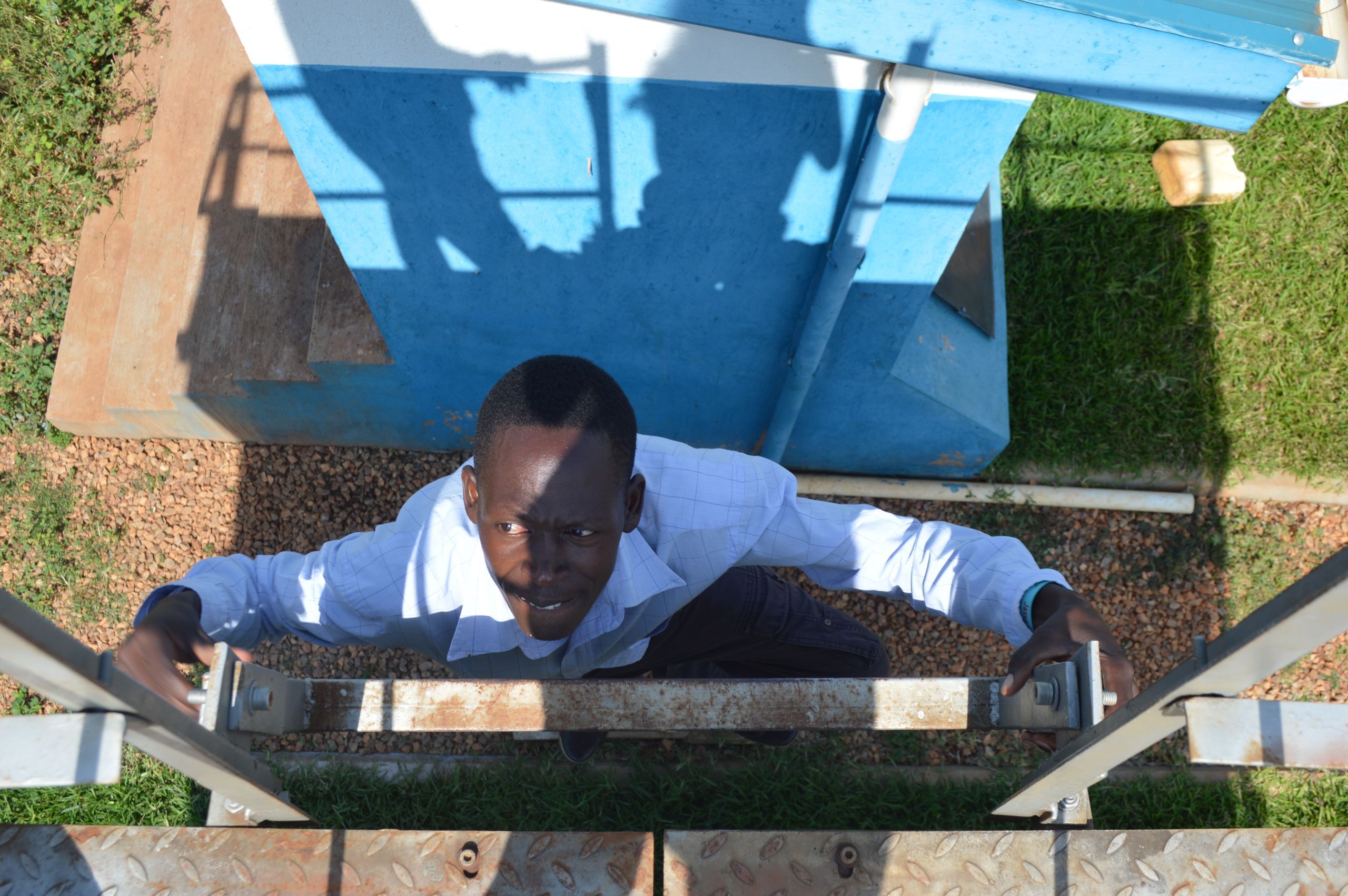 Christopher Damba of Walumbe Village climbing up to a water tower in Nakalanga. His daughter recently died when she could not make it to a hospital in time to receive treatment. Image by Annika McGinnis. Uganda, 2019.