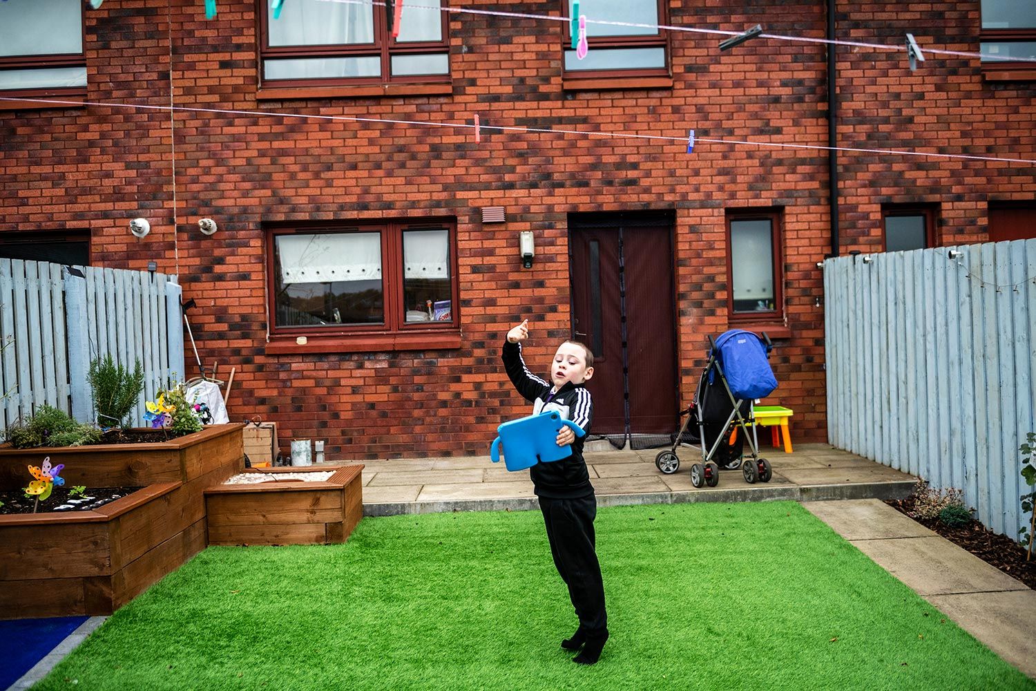 David Crichton plays on his iPad in the backyard of his home, where he has a sensory garden, in Possilpark. Image by Michael Santiago. United Kingdom, 2019.