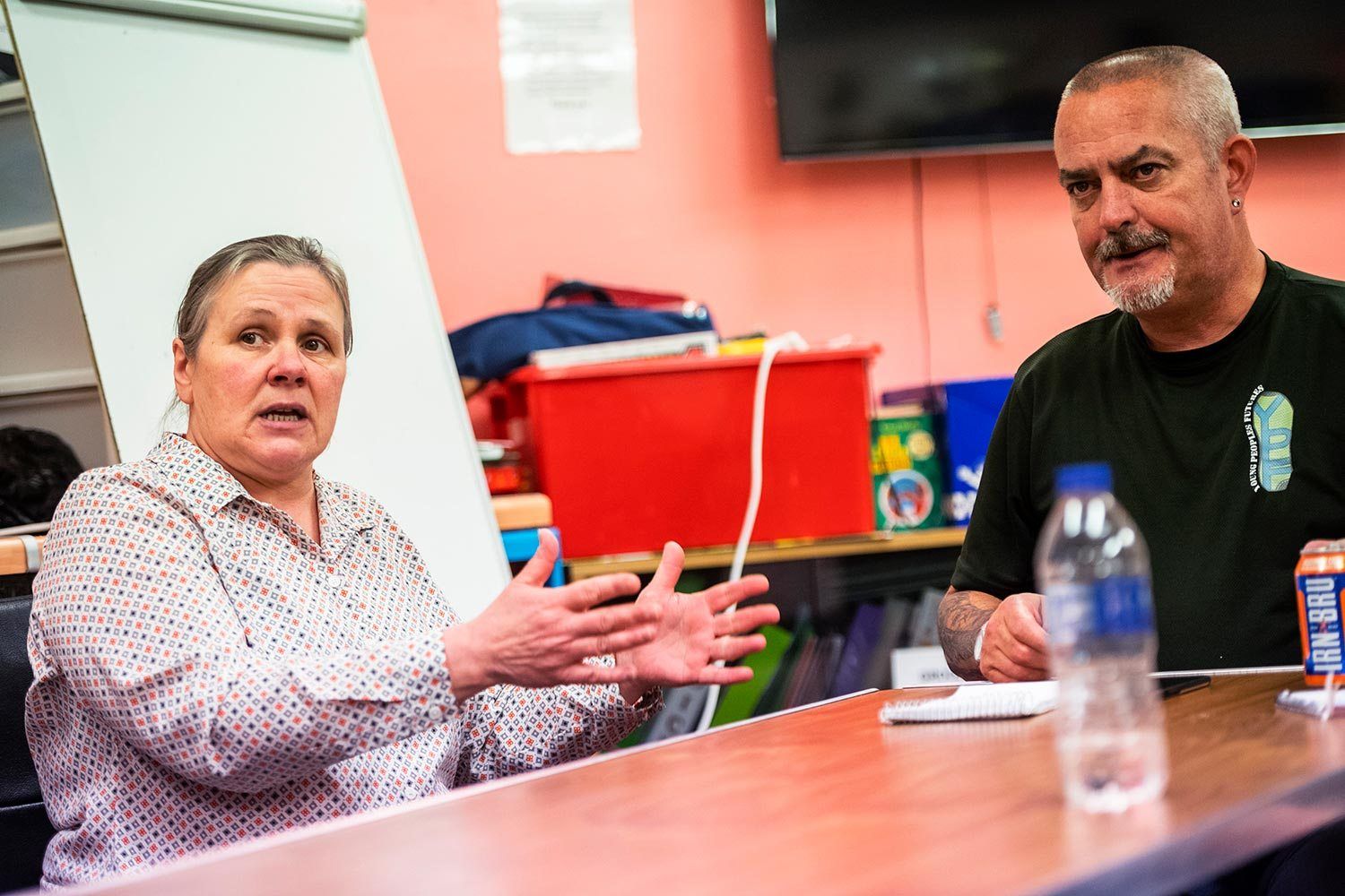 Ann Lawrance, project manager at Young People’s Futures, speaks about the work her organization does in the community as Frank Law, staff member with YPF’s family support service, looks on at Possilpoint Community Centre. Image by Michael Santiago. United Kingdom, 2019.