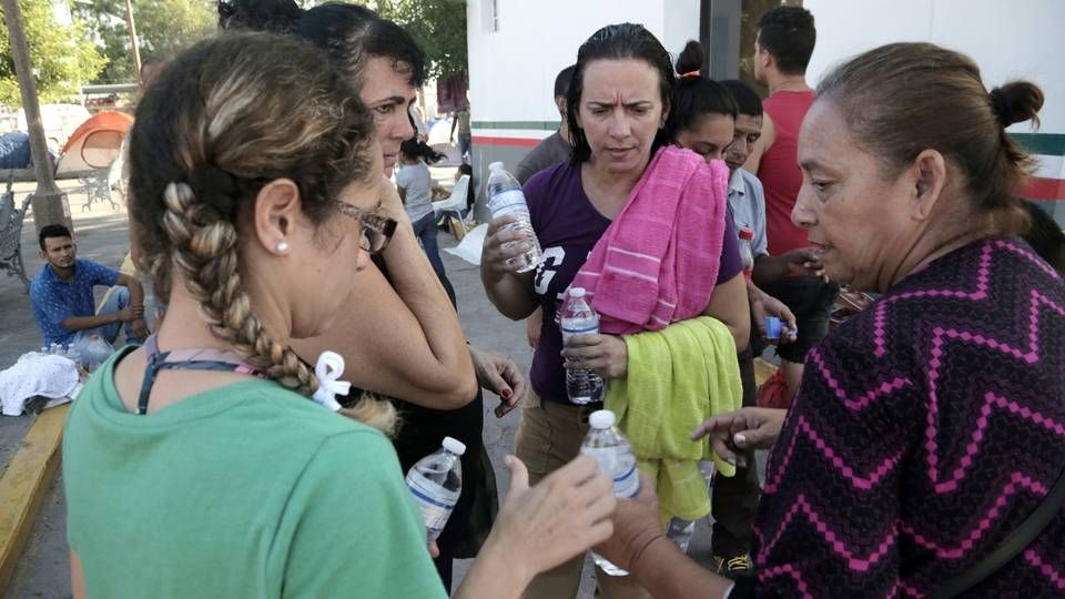 A Mexican volunteer, right, gives water to Cuban migrant women living in a makeshift camp by the Gateway International Bridge in Matamoros, Mexico. Image by Jose A. Iglesias. Mexico, 2019.