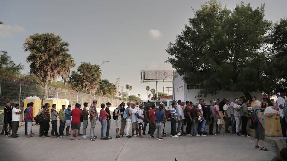 Migrants line up for food at a camp located on the Matamoros, Mexico, side of the Gateway International Bridge that connects Matamoros to Brownsville, Texas. Church and volunteer organizations in Brownsville provide water and food for the migrants on the Mexican side of the border as they wait for their asylum requests to be processed. Image by Jose A. Iglesias. Mexico, 2019.