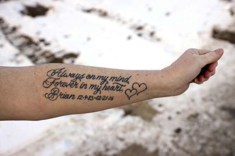 Amy Fischer shows a tattoo that she got after her son Brian, 33, died by suicide in 2016. “I had someone ask me the other day, ‘Does it get any easier?’” Amy said about her grieving, tears forming in her eyes. “I said, ‘It gets easier to cover it.’” Image by Coburn Dukehart / Wisconsin Watch. United States, 2020.