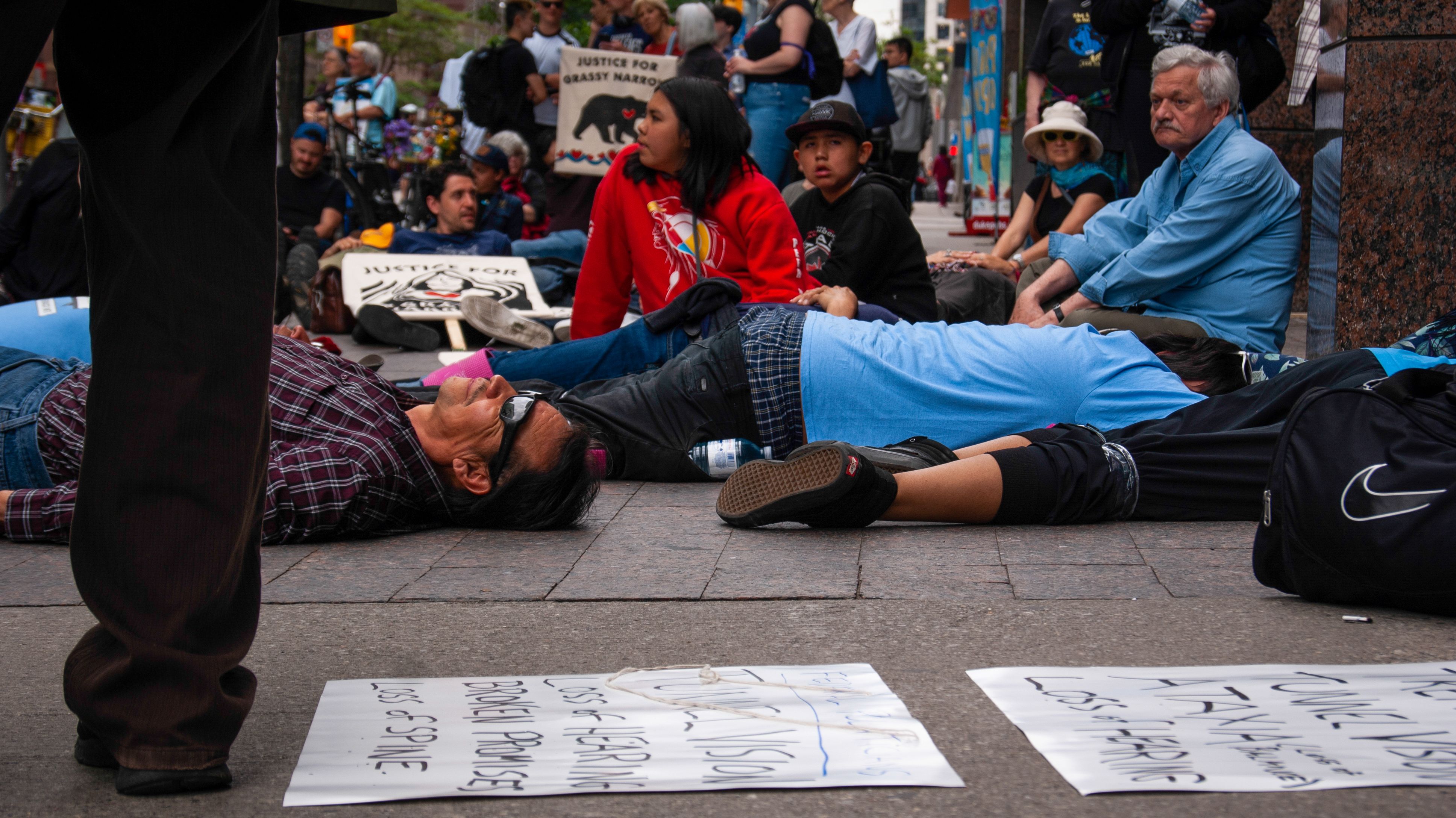 Residents of Grassy Narrows and their supporters lie on the ground in front of the Indigenous Services Canada Office in Toronto. The community organized a "die-in" in front of the office to remind the Canadian government of their suffering. Image by Shelby Gilson. Canada, 2019.