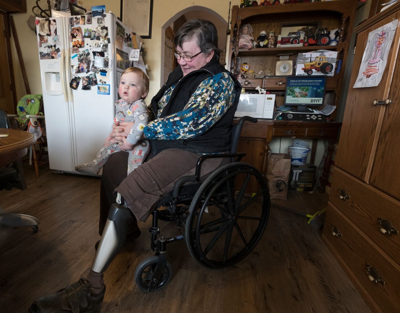Cathy Mess holds her 10-month-old grandson, Ben. Mess used to help with many of the chores on the farm before she lost her left leg in a farm accident. Image by Mark Hoffman. United States, 2019.